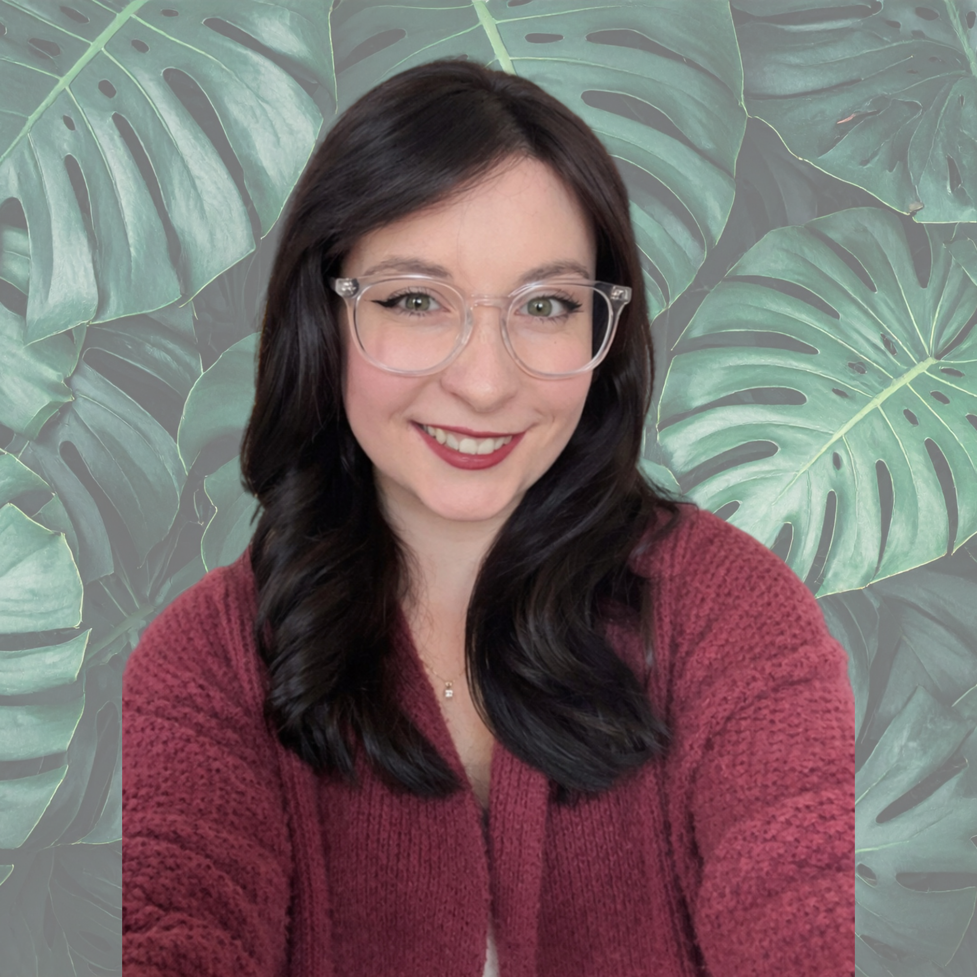 A woman with long dark hair and glasses smiling at the camera, wearing a maroon sweater, with colorful mountain and forest mural and string lights in the background.