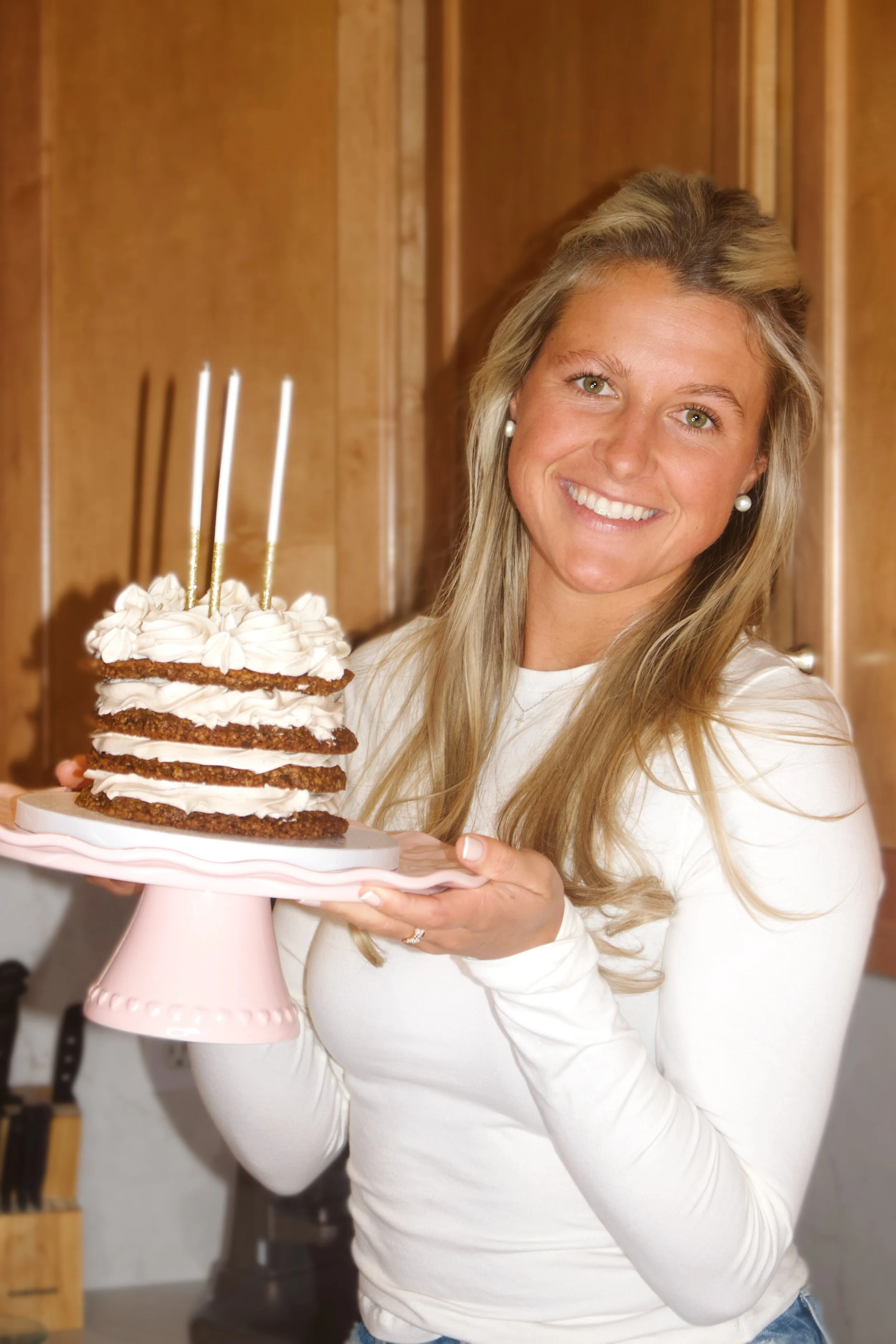 Woman holding a layered cookie cake with candles, smiling at the camera.