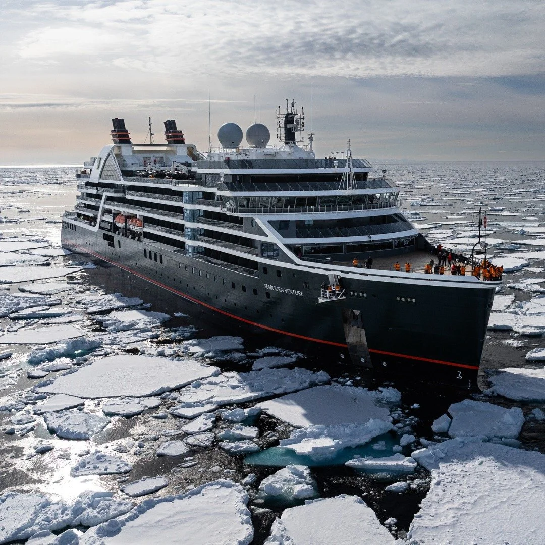 A large cruise ship navigating through icy waters with floating ice chunks, under a cloudy sky.