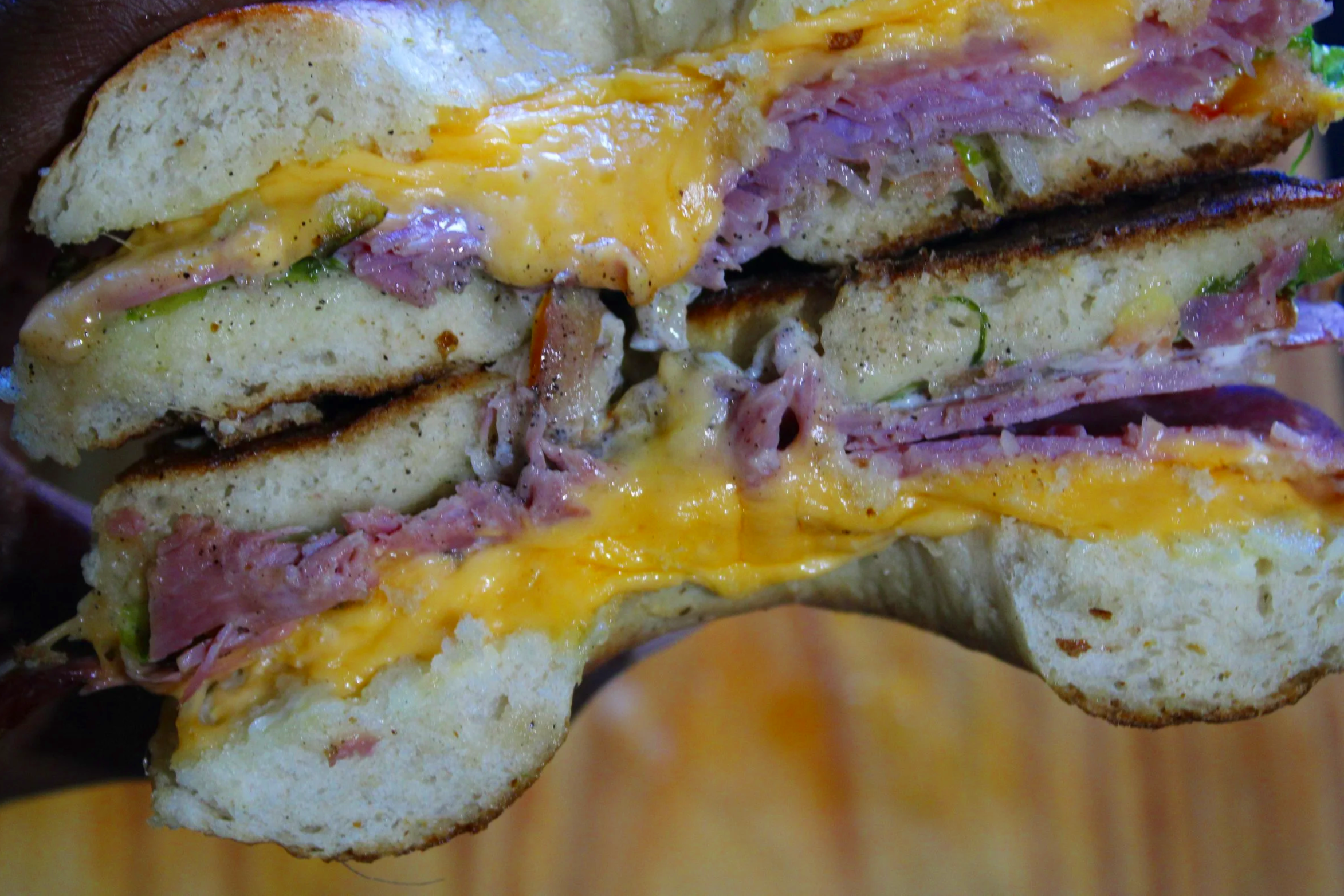 Close-up of a Sourdough Bagel cut in half, with cheese, Pepper Beef, and salad inside 