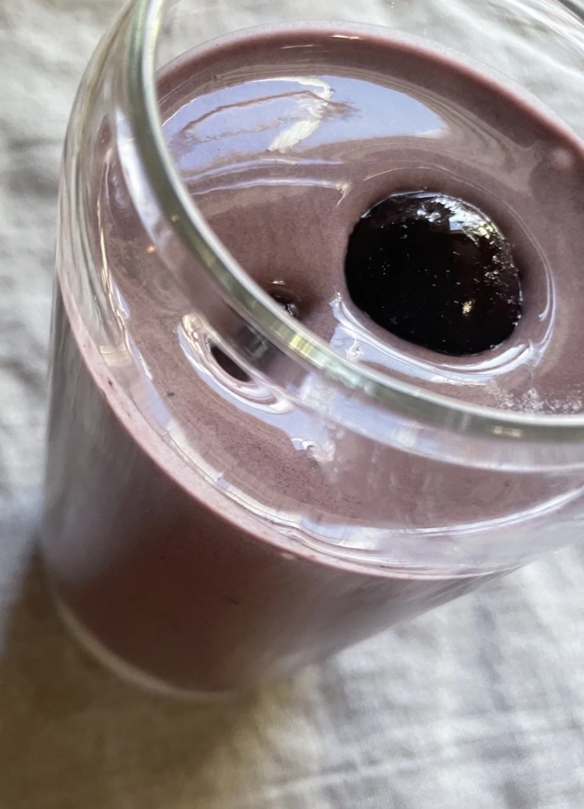 Close-up of a glass filled with purple smoothie topped with two dark berries.