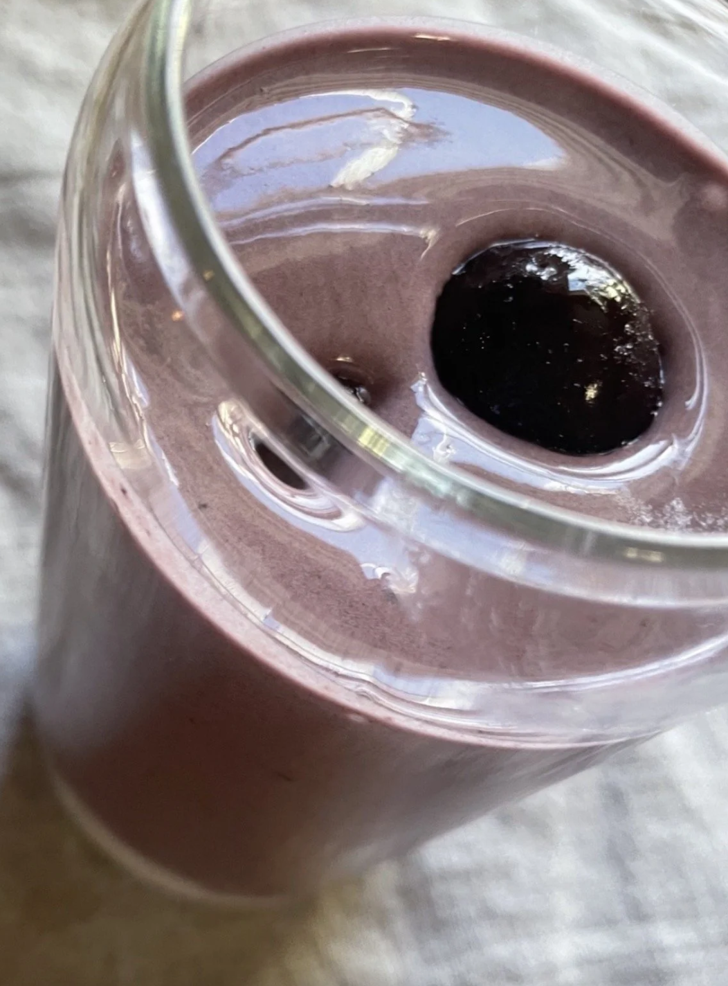 Close-up of a glass of dark purple or black-colored beverage with ice cubes on top.