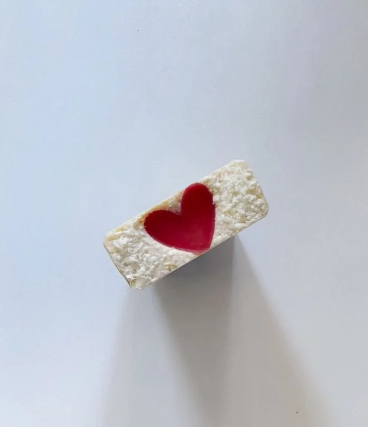 A rectangular white bar with a red heart design on top, placed on a white surface, casting a shadow.