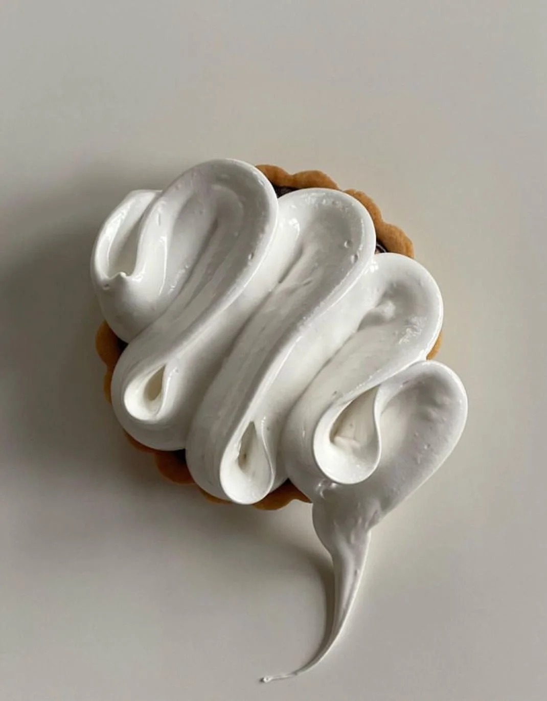 A dessert with a cookie base topped with white whipped cream in an artistic swirl.
