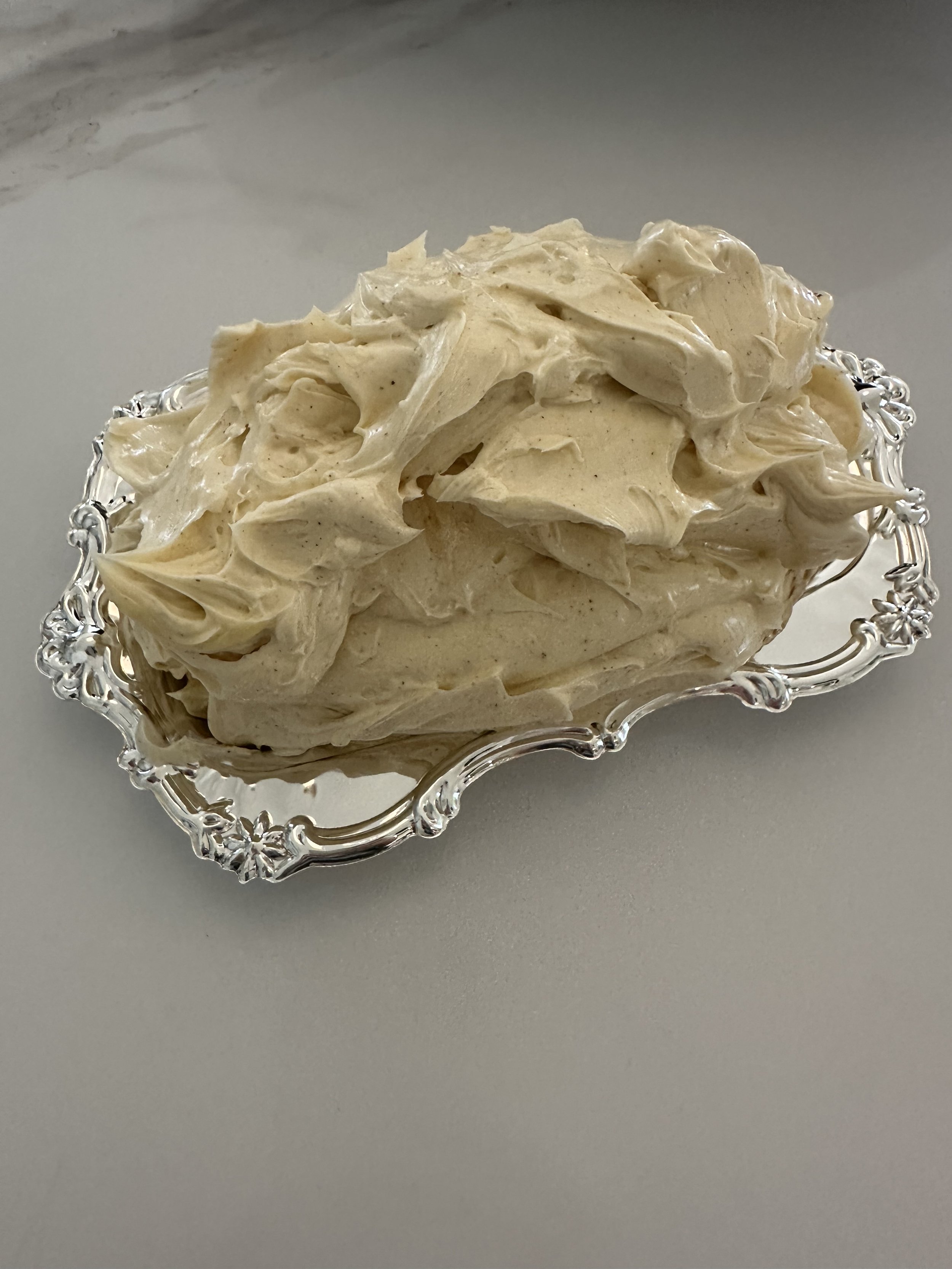 A silver ornate dish filled with a generous serving of creamy, textured chocolate chip cookie dough.