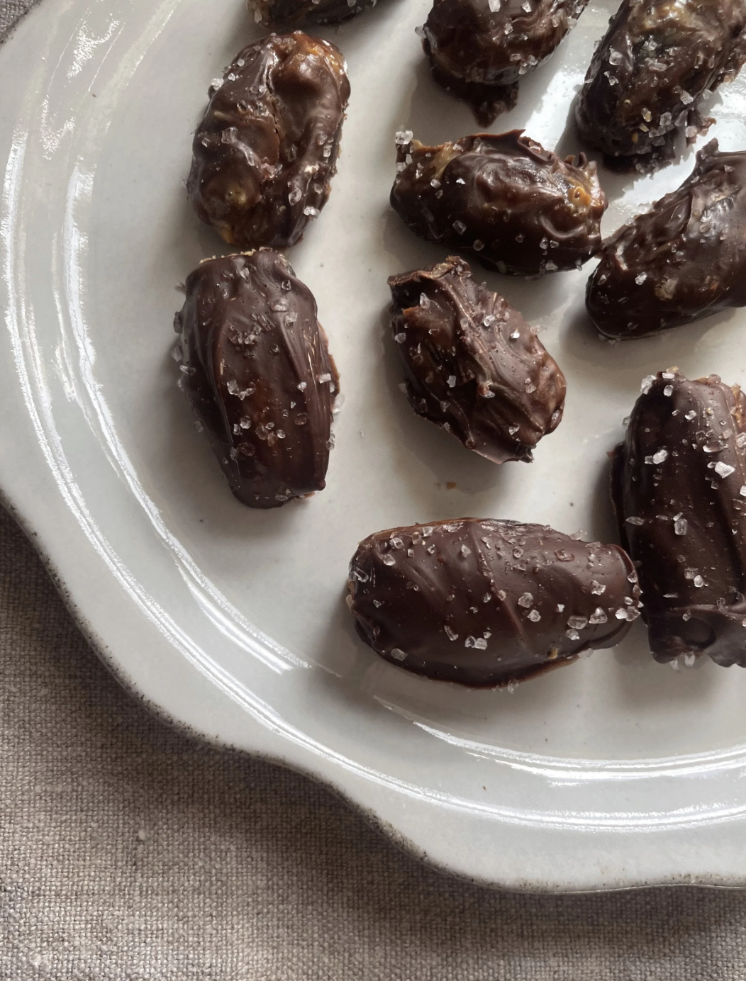 Close-up of chocolate-covered dates sprinkled with sea salt on a white plate.