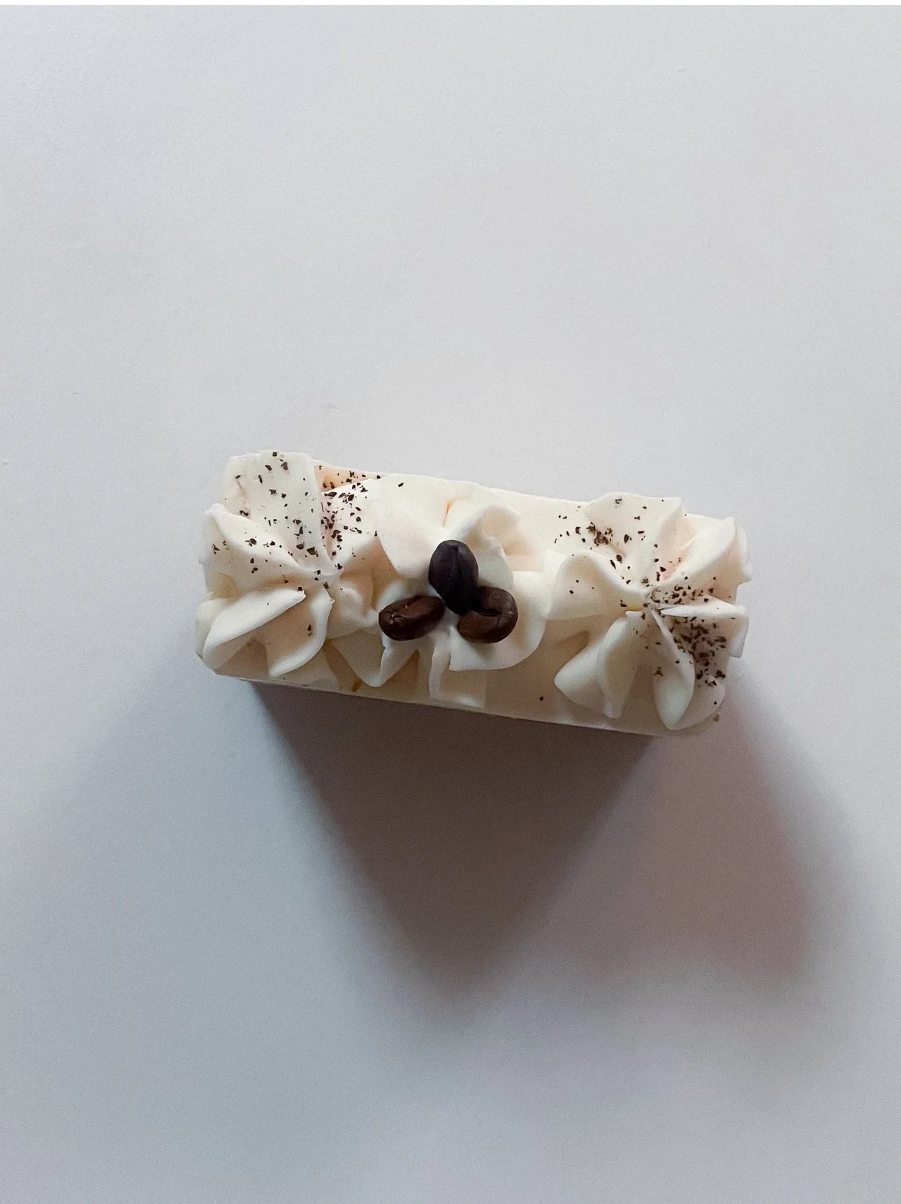 A rectangular slice of white cake with white frosting, decorated with three coffee beans and sprinkled with cocoa powder, on a white surface.