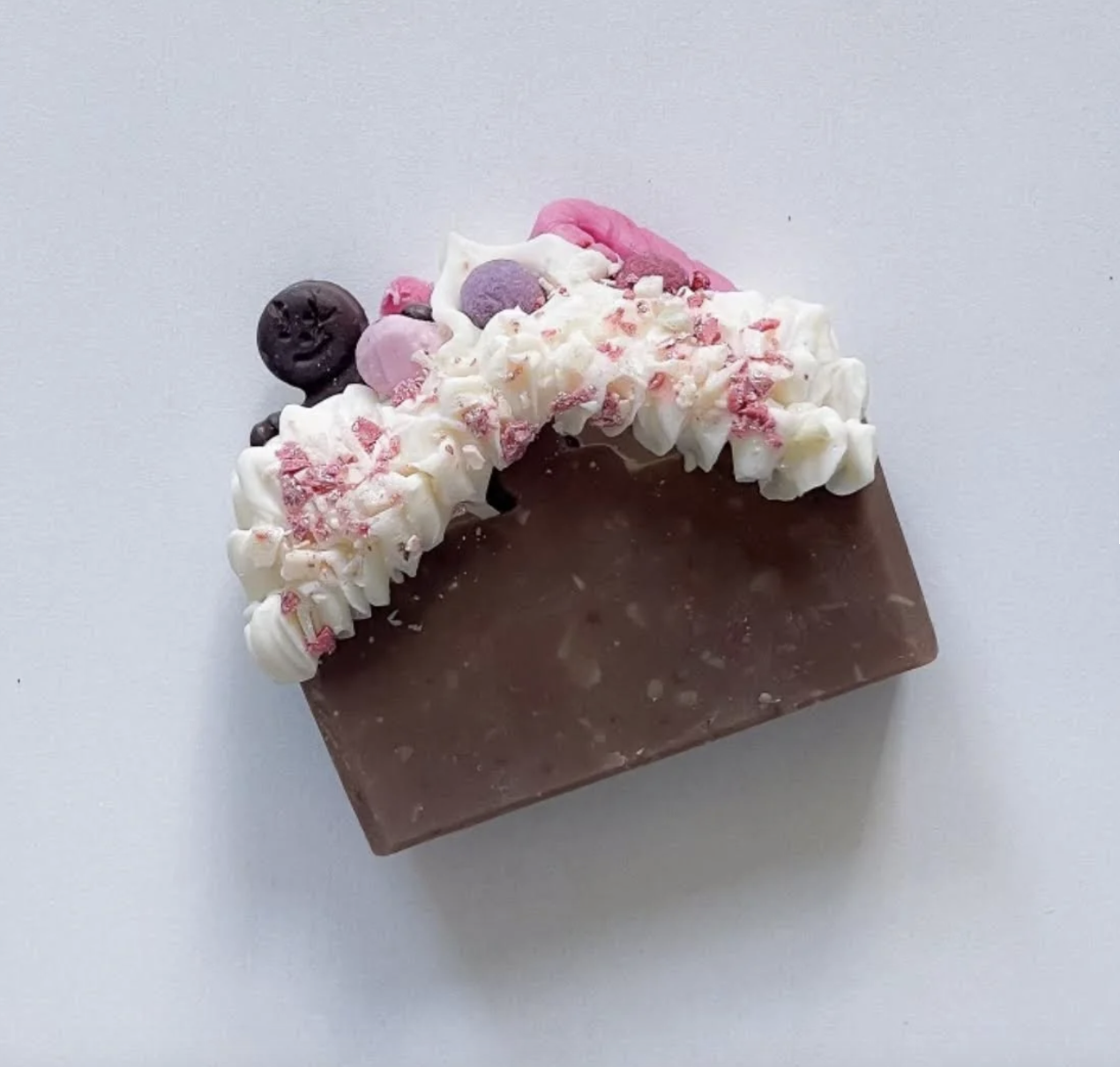 A chocolate bar topped with whipped cream, blueberries, pink and purple candies, and pink sprinkles, shaped like a crescent moon.