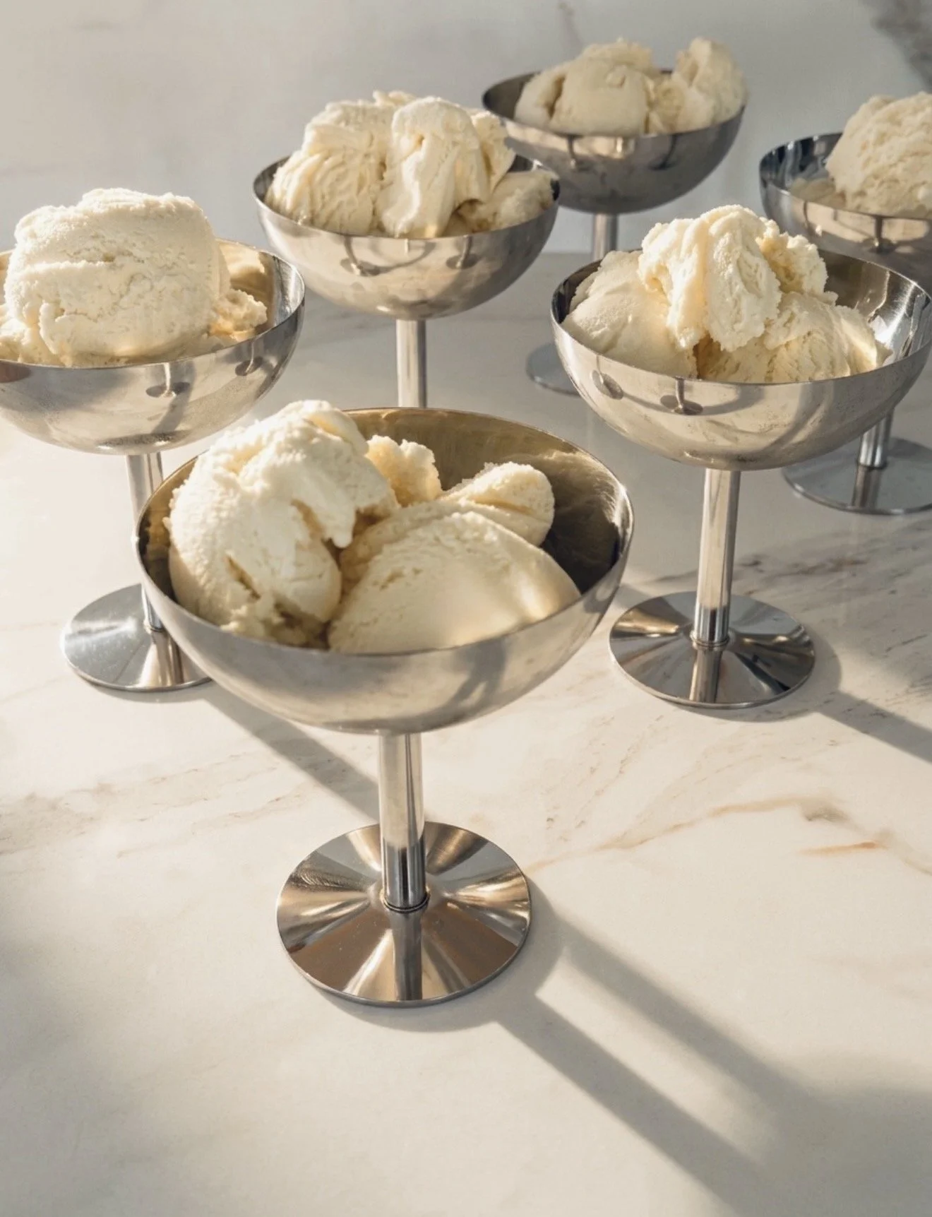 Six silver bowls filled with scoops of vanilla ice cream on a marble countertop, arranged in two rows of three.