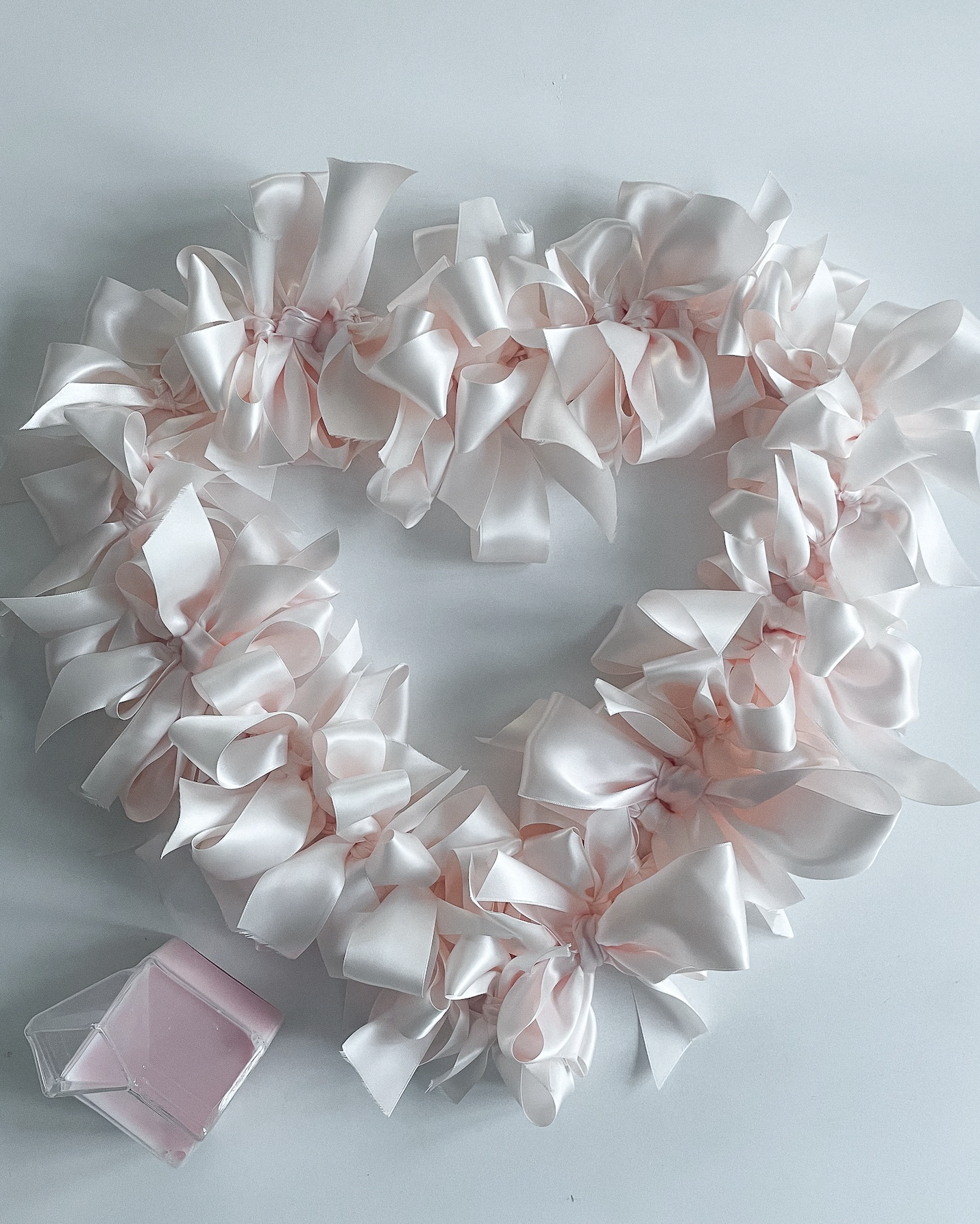 Pink satin ribbon bow decorative wreath with a small pink candle in a glass holder.