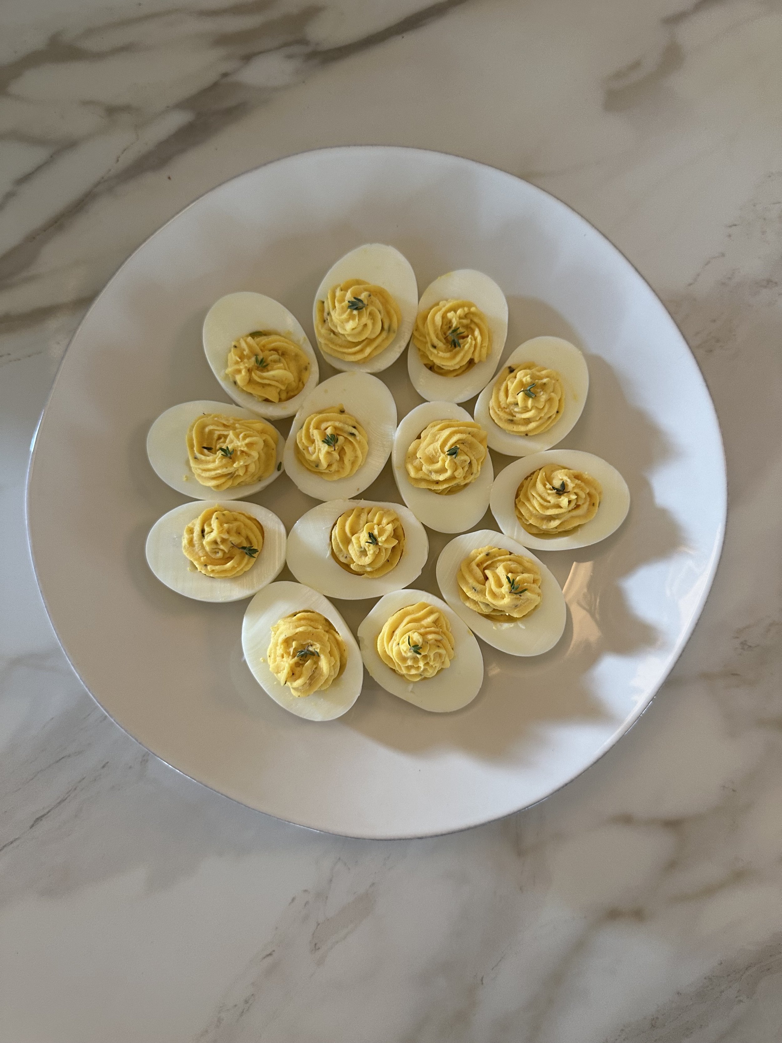 A white plate with halved hard-boiled eggs topped with yellow egg yolk salad, garnished with small green herbs, on a marble surface.