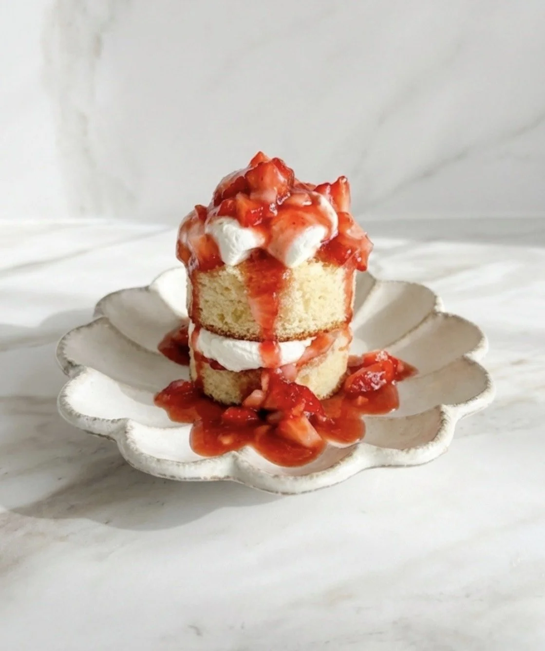 Strawberry shortcake on a white plate with strawberry compote and whipped cream.