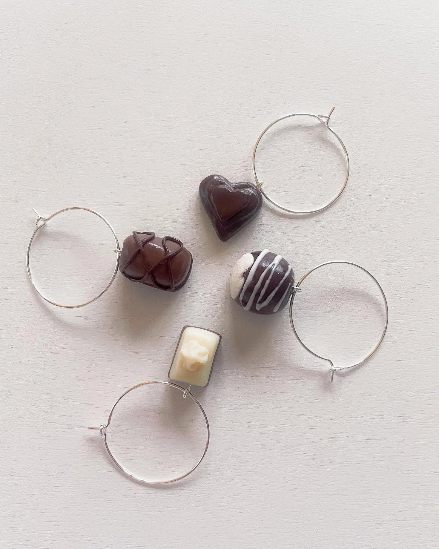 Four metal hoop earrings with different chocolate charms on a white surface.