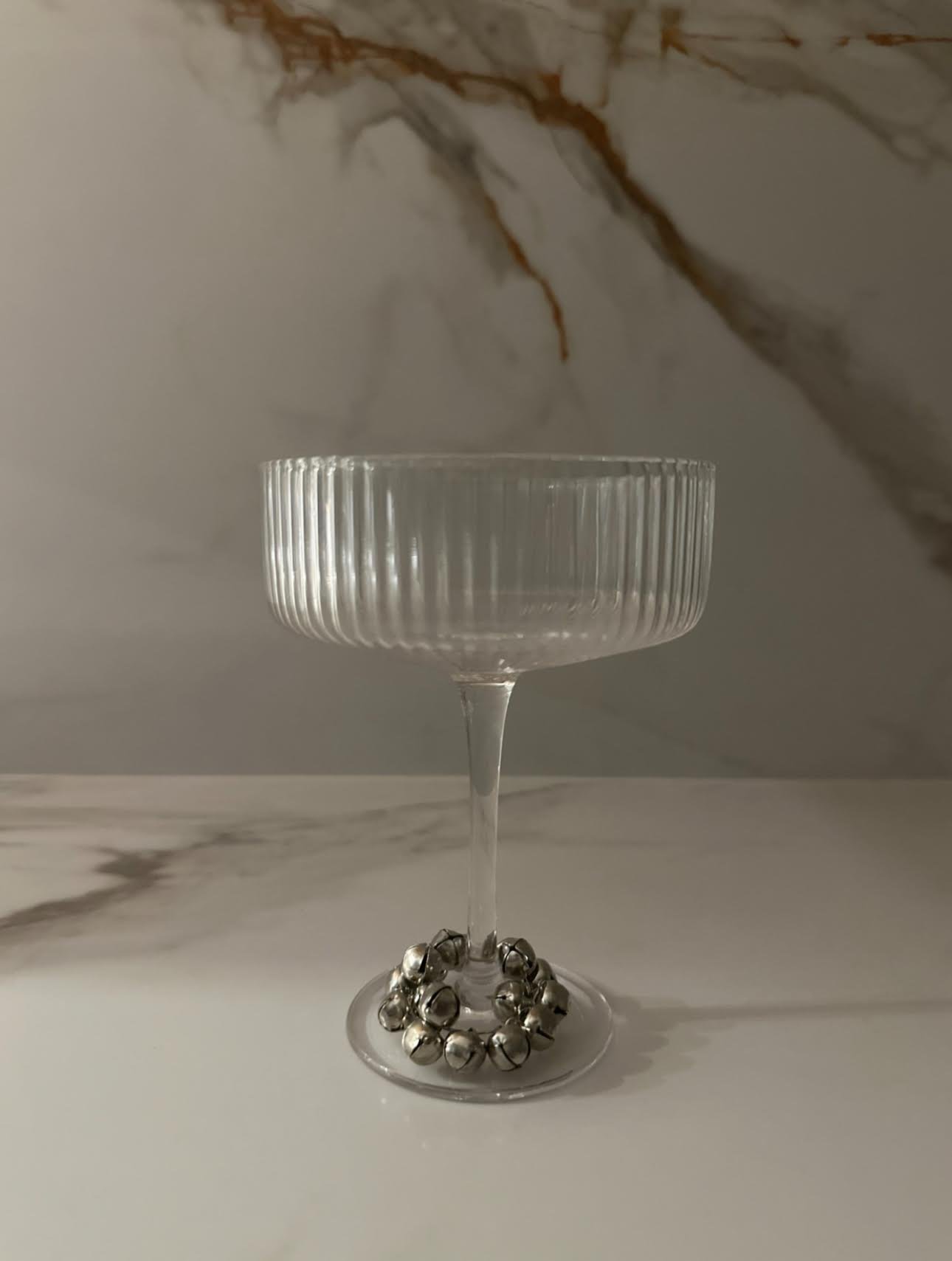 Empty glass goblet with a fluted design on the bowl, a slender stem, and a round base, placed on a white marble surface with gray and brown veining.