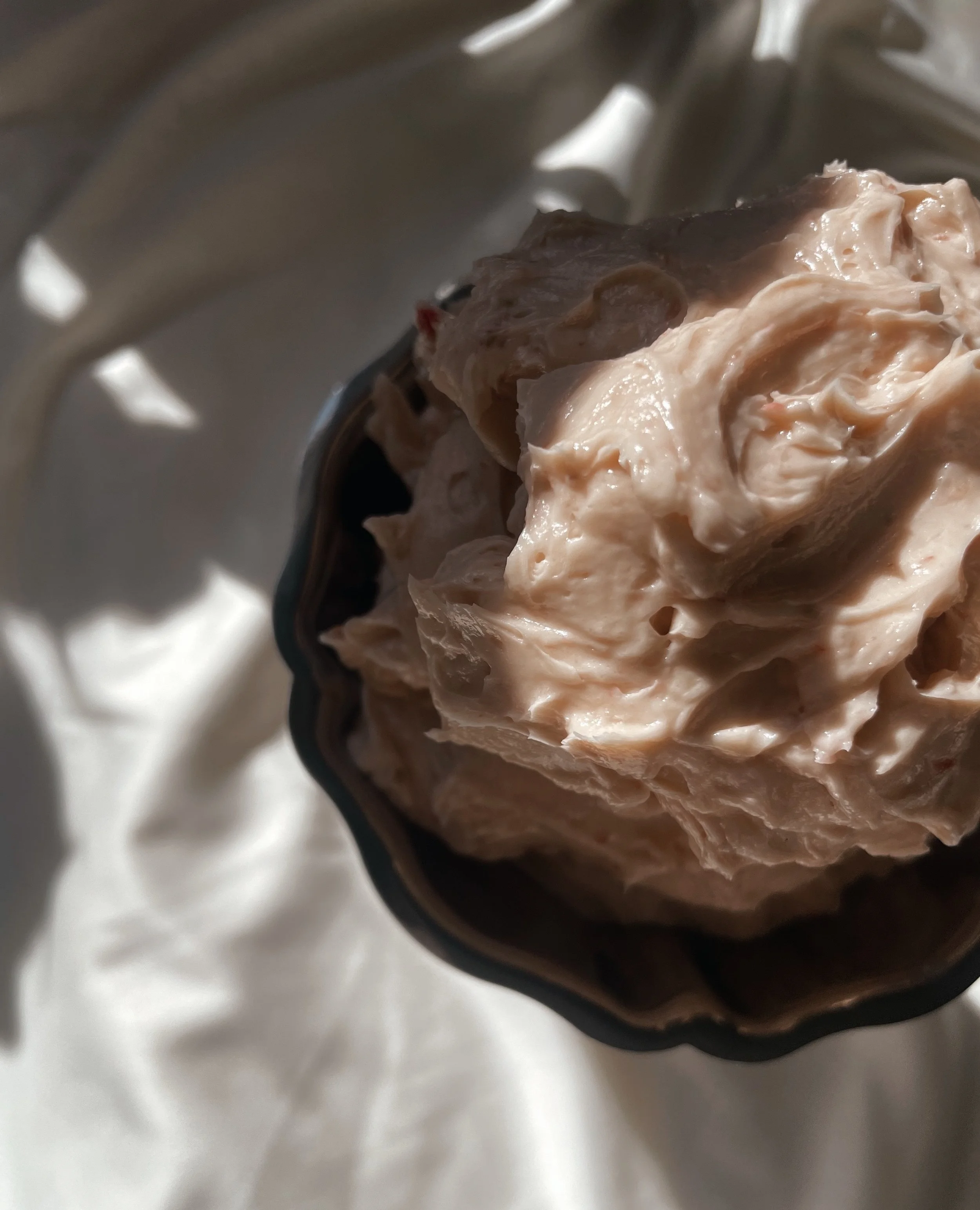 Close-up of a spoonful of whipped or creamy food, possibly ice cream or dessert, held above a reflective silver bowl or container.