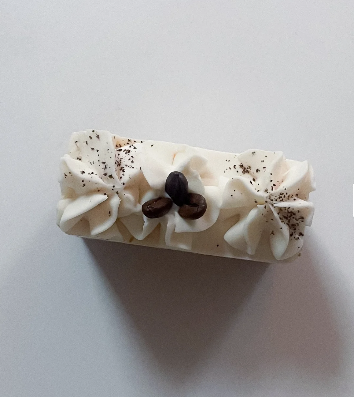 A rectangular cake with white frosting, decorated with whipped cream, coffee beans, and sprinkled with chocolate shavings.