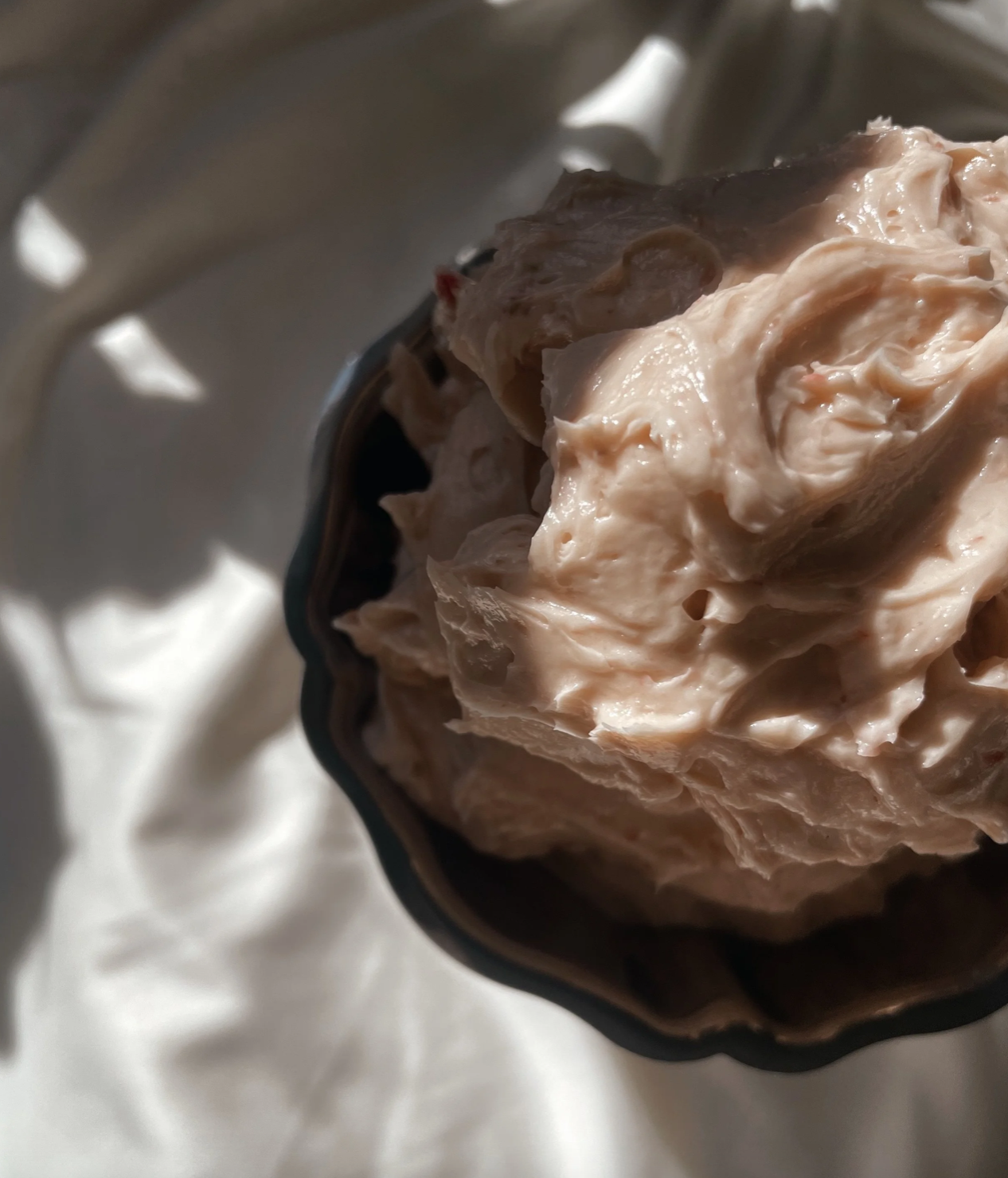 Close-up of a bowl filled with creamy, pinkish topping or spread, illuminated by natural light.