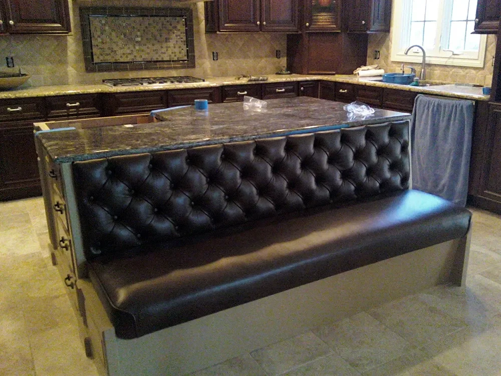 Kitchen with dark wood cabinets, granite countertops, and a built-in stovetop. A kitchen island features a leather tufted back and seating.