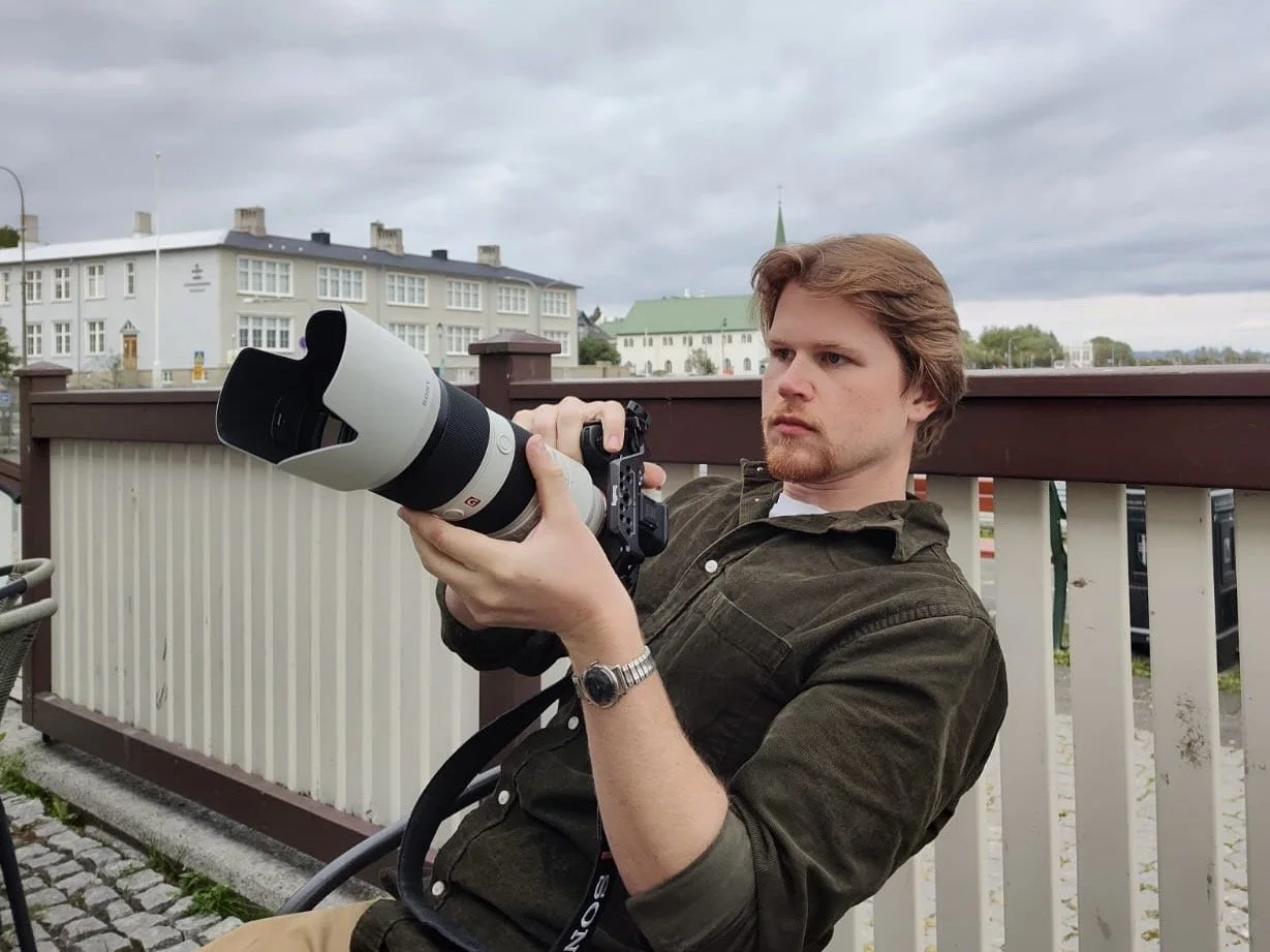 Billy sitting at a wedding wielding his professional Sony camera and a telephoto lens.