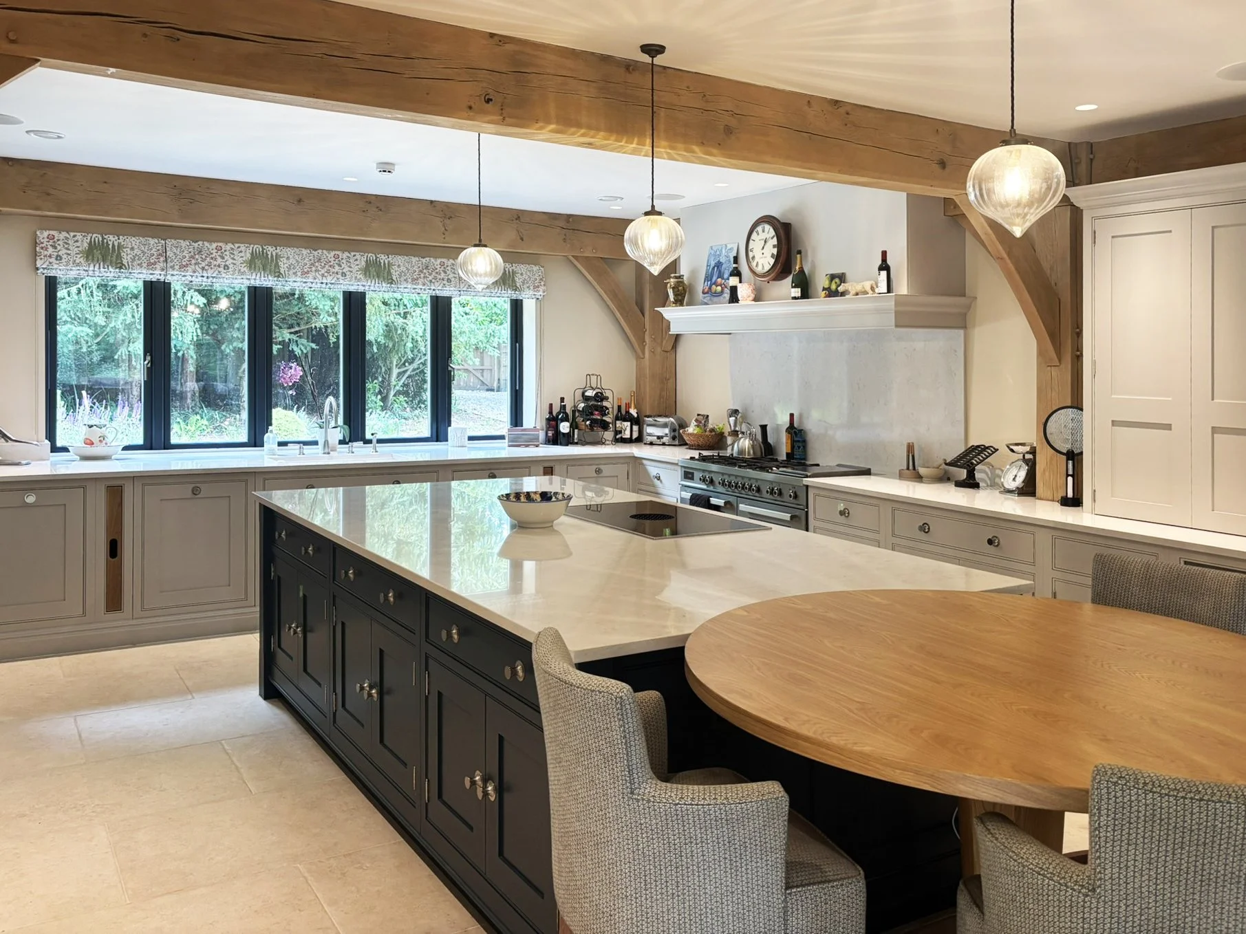 Sarsen Architects — Kitchen with large cream-colored island, black base, and white marble countertop. Round wooden dining table with four chairs. Large window with floral