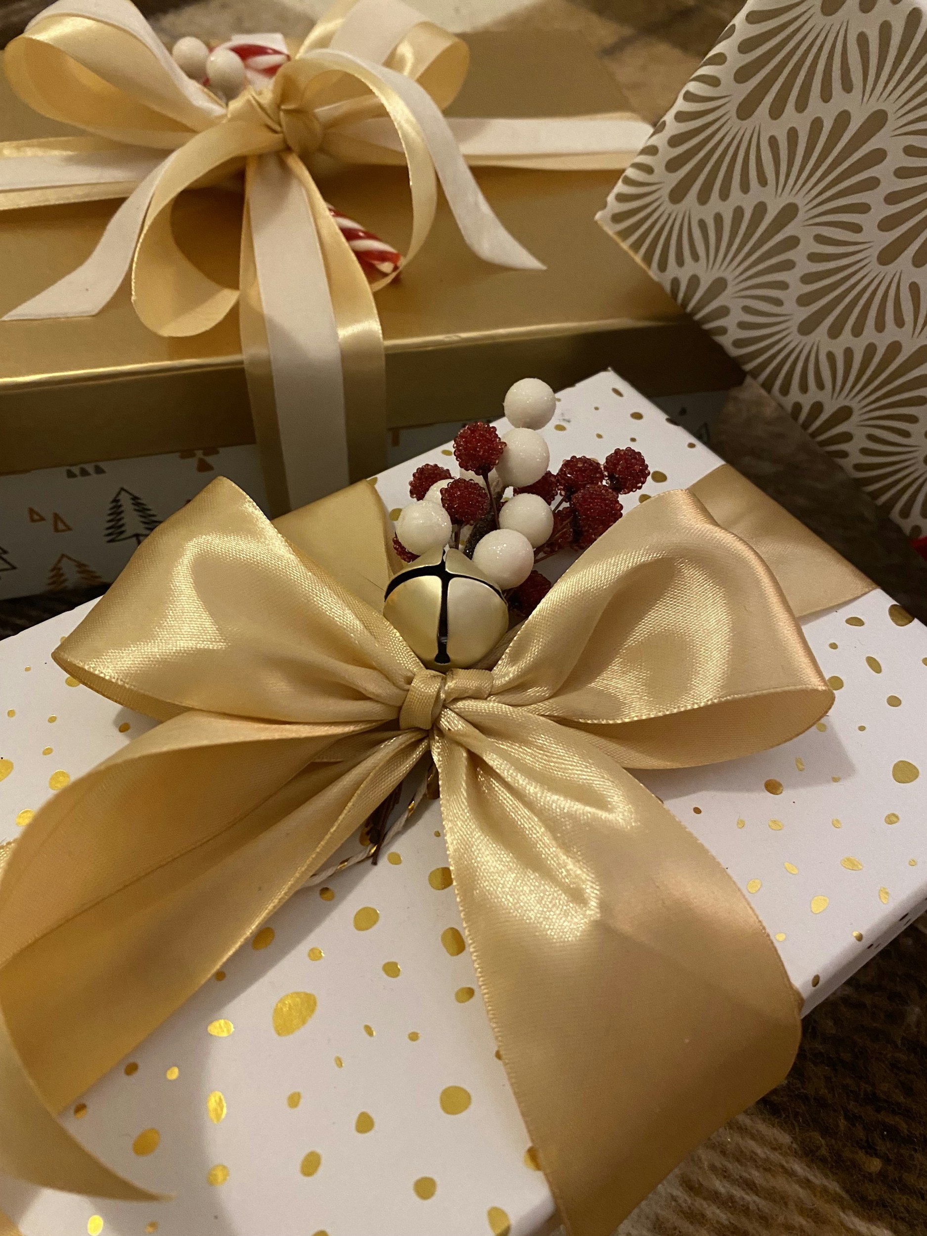 Holiday gift boxes decorated with large gold ribbons, gold polka dot wrapping paper, and festive ornaments including white and red berries.