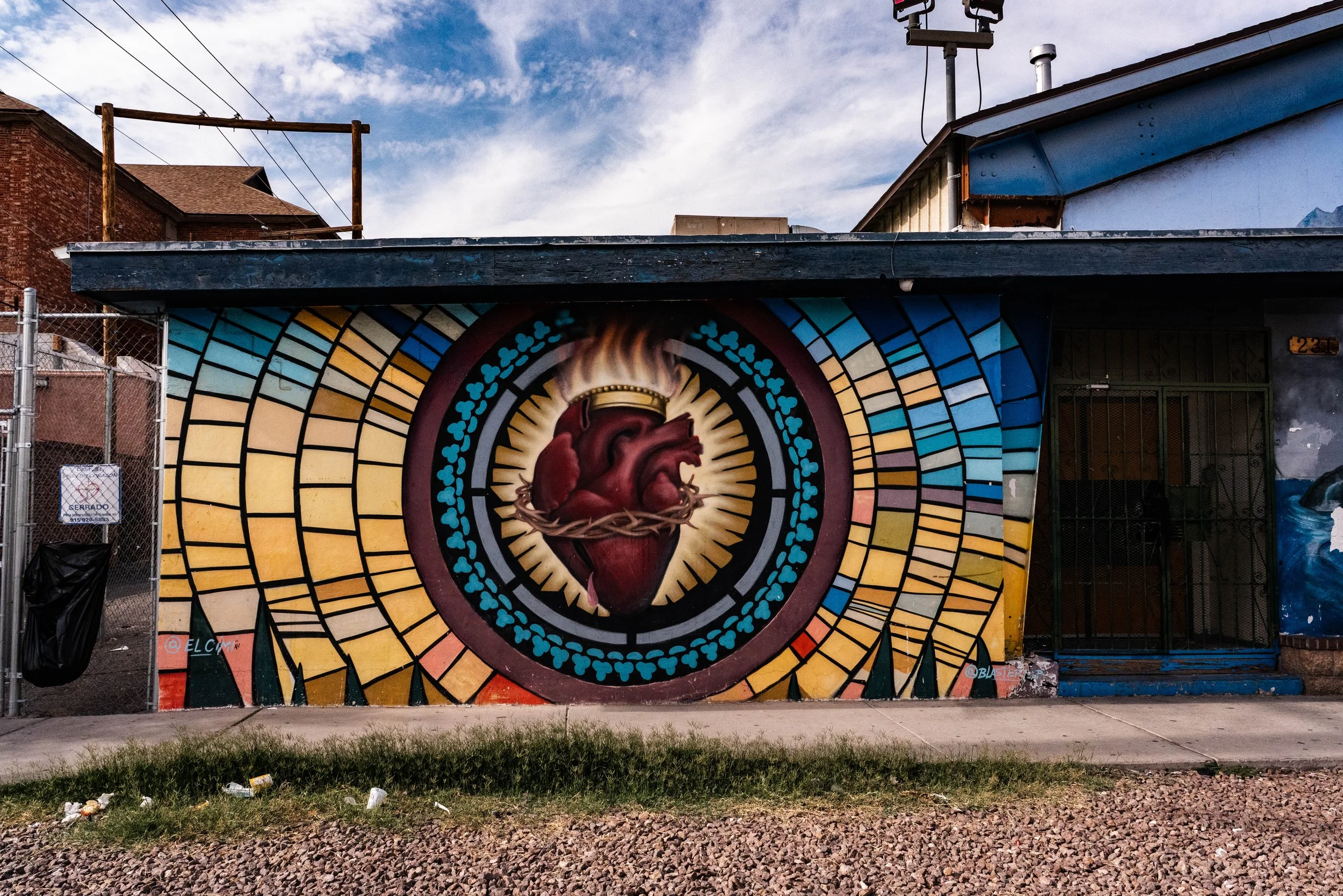 Colorful mural of a detailed human heart with a crown of thorns around it on an exterior wall of a building, with vibrant geometric patterns radiating outward.