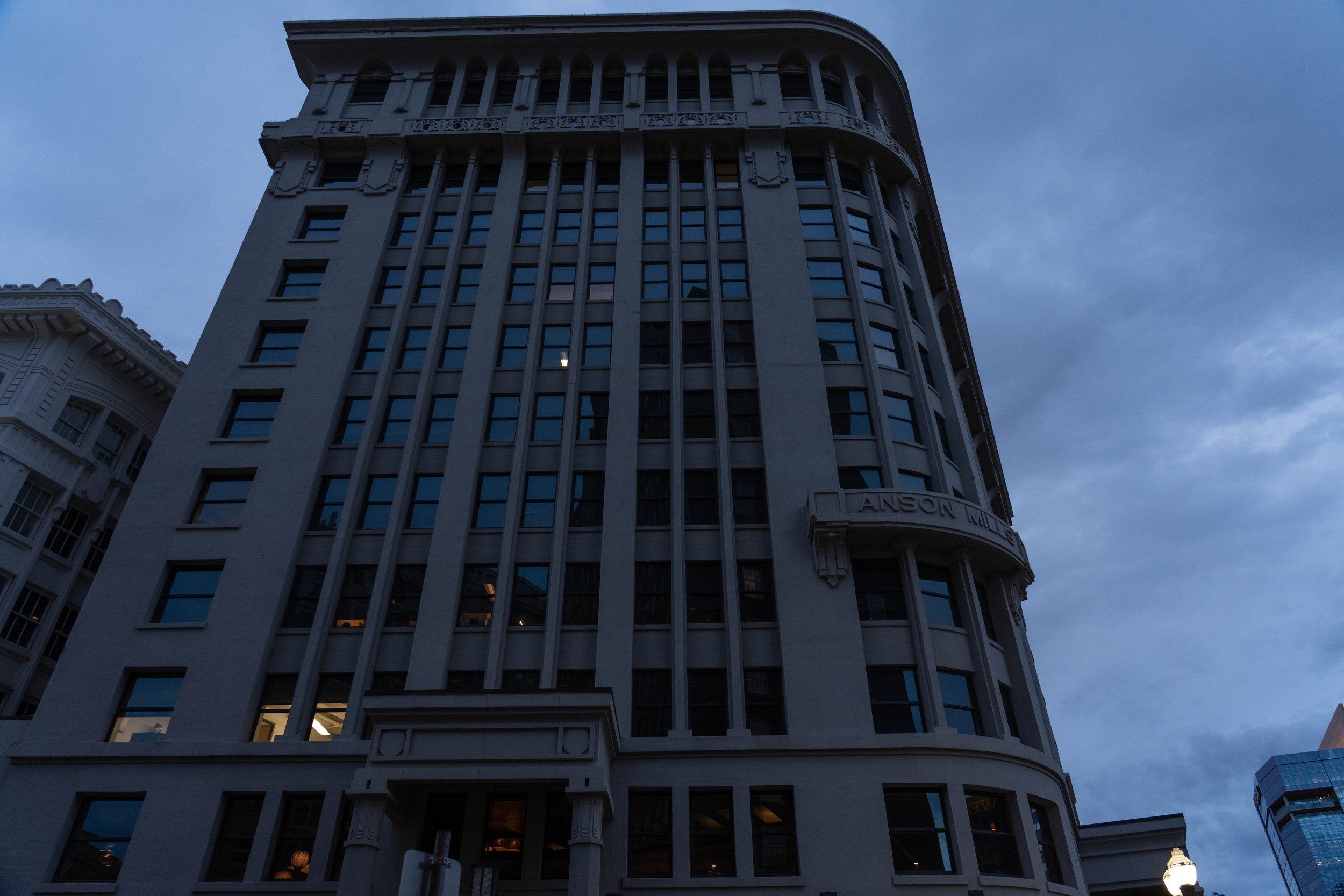 A tall, historic building with multiple windows, named 'Anson Mills,' on a cloudy evening in an urban setting.