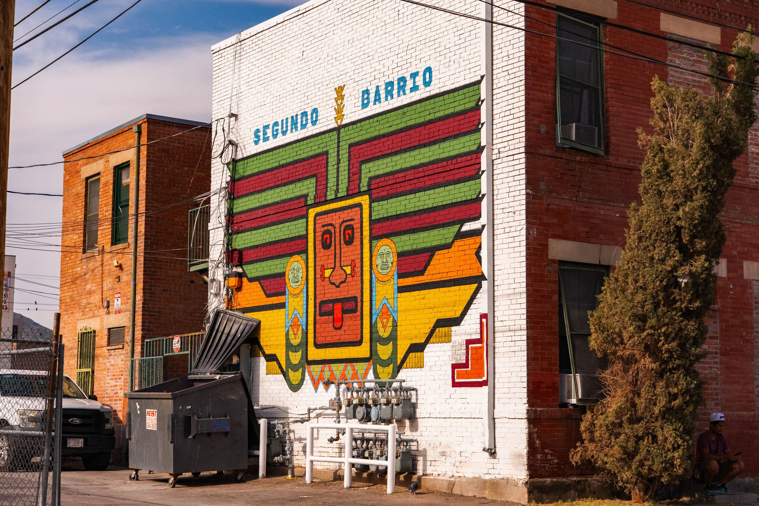 Colorful mural of a native face painted on the side of a brick building, with the words "Segundo Barrio" written above.