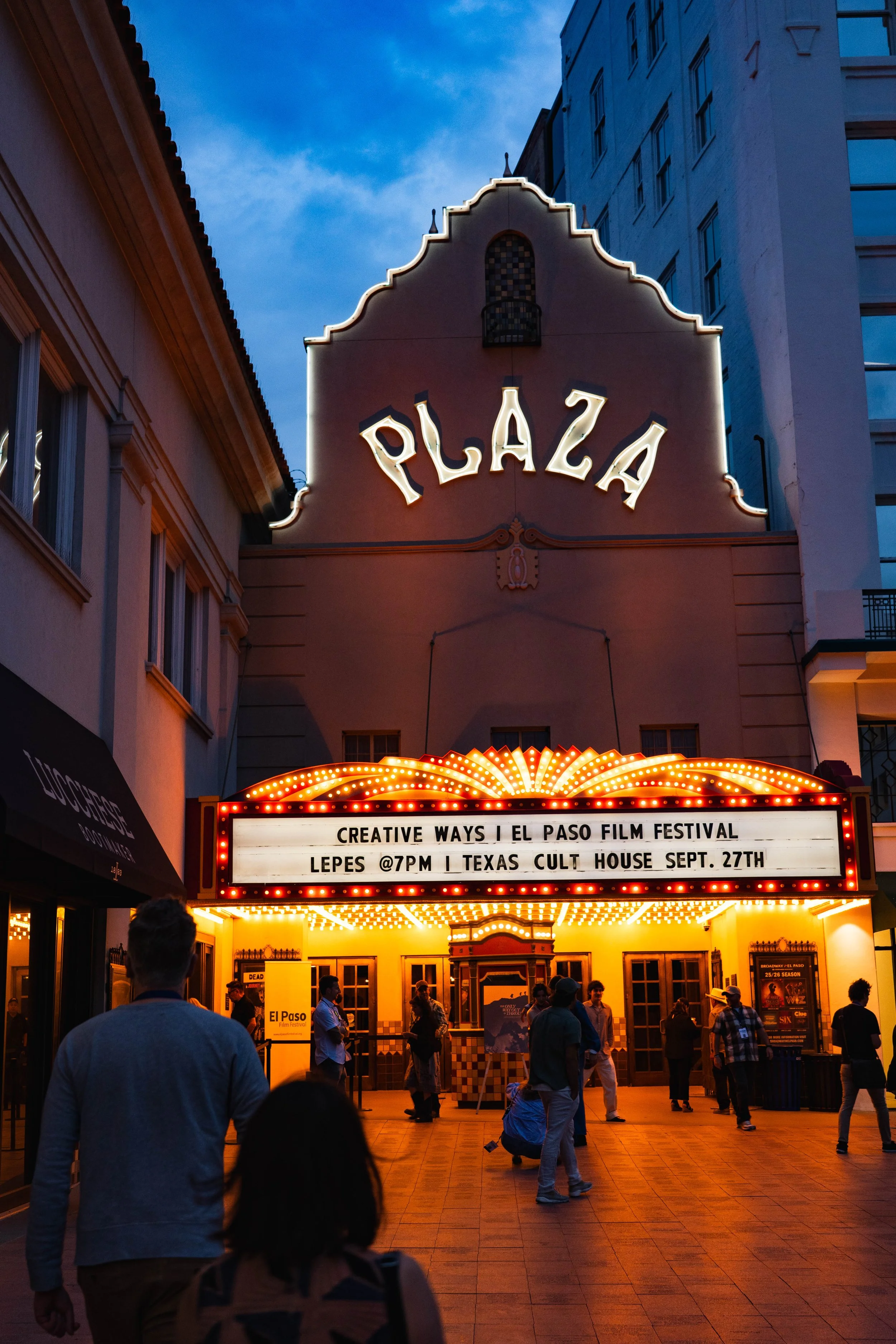 People walking in front of the El Paso Plaza Theatre at dusk, with illuminated marquee advertising a film festival and concert event.