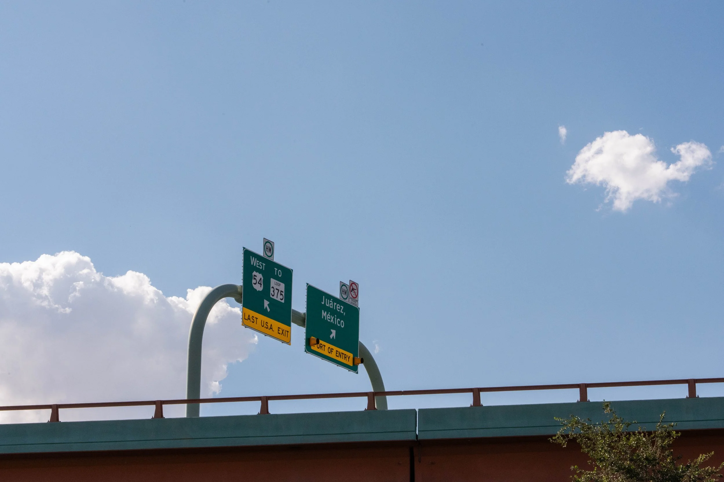 Highway signs indicating directions to Juárez, Mexico, and US routes 54 and 375, with clear blue sky and clouds in the background.