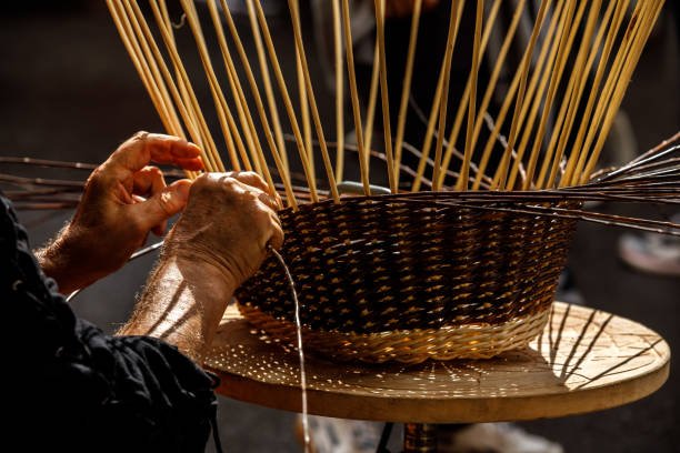 Hands weaving a wicker basket with long wooden sticks inside.