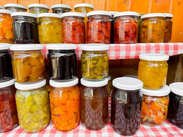 Several jars of canned vegetables and fruits arranged on a table with a checkered tablecloth.