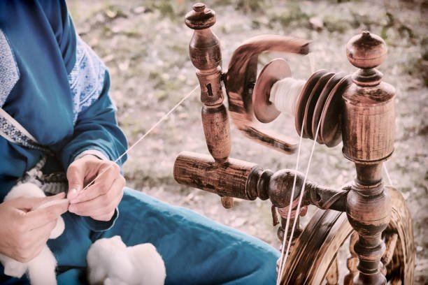 Person using a spinning wheel to spin yarn outdoors.
