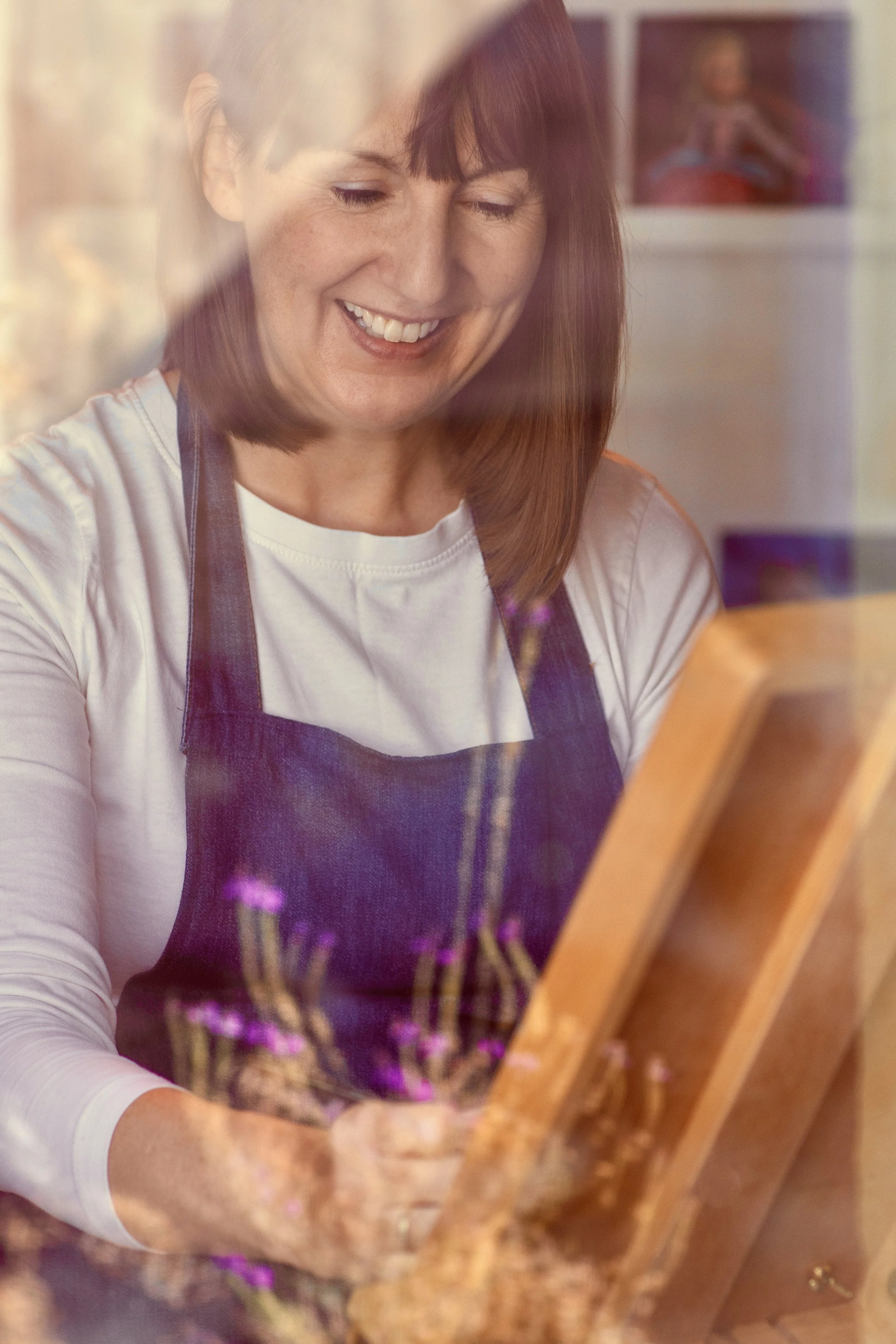 A woman with brown hair wearing a white shirt and a dark apron is looking at a menu or tablet, smiling.