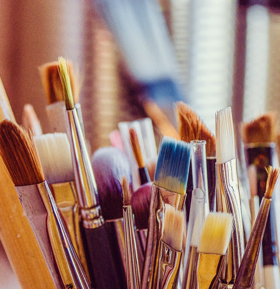 A collection of paintbrushes of various sizes and colors in a container, with a blurred background.