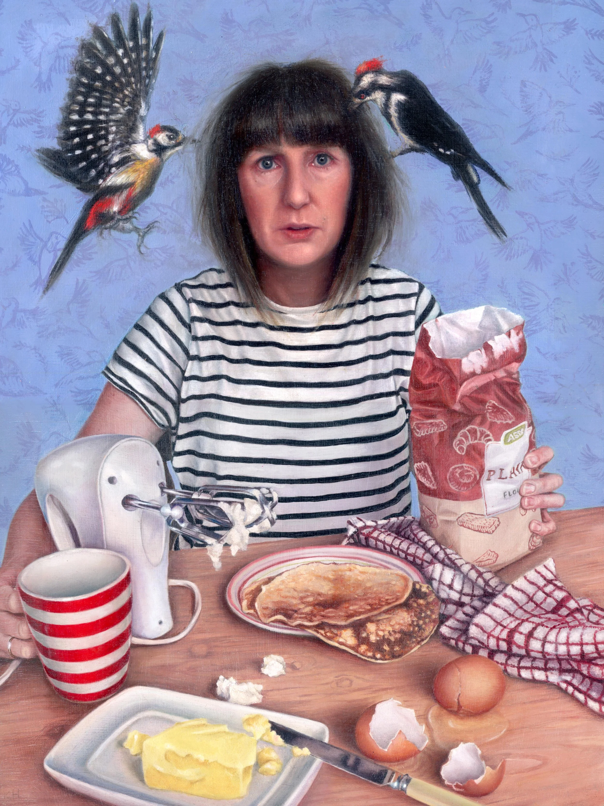 A woman with dark hair and bangs wearing a striped shirt sitting at a table with breakfast foods, including an egg, butter, and a plate of pancakes. She holds a bag of flour in one hand and a mixing attachment in the other. Two woodpecker are flying 