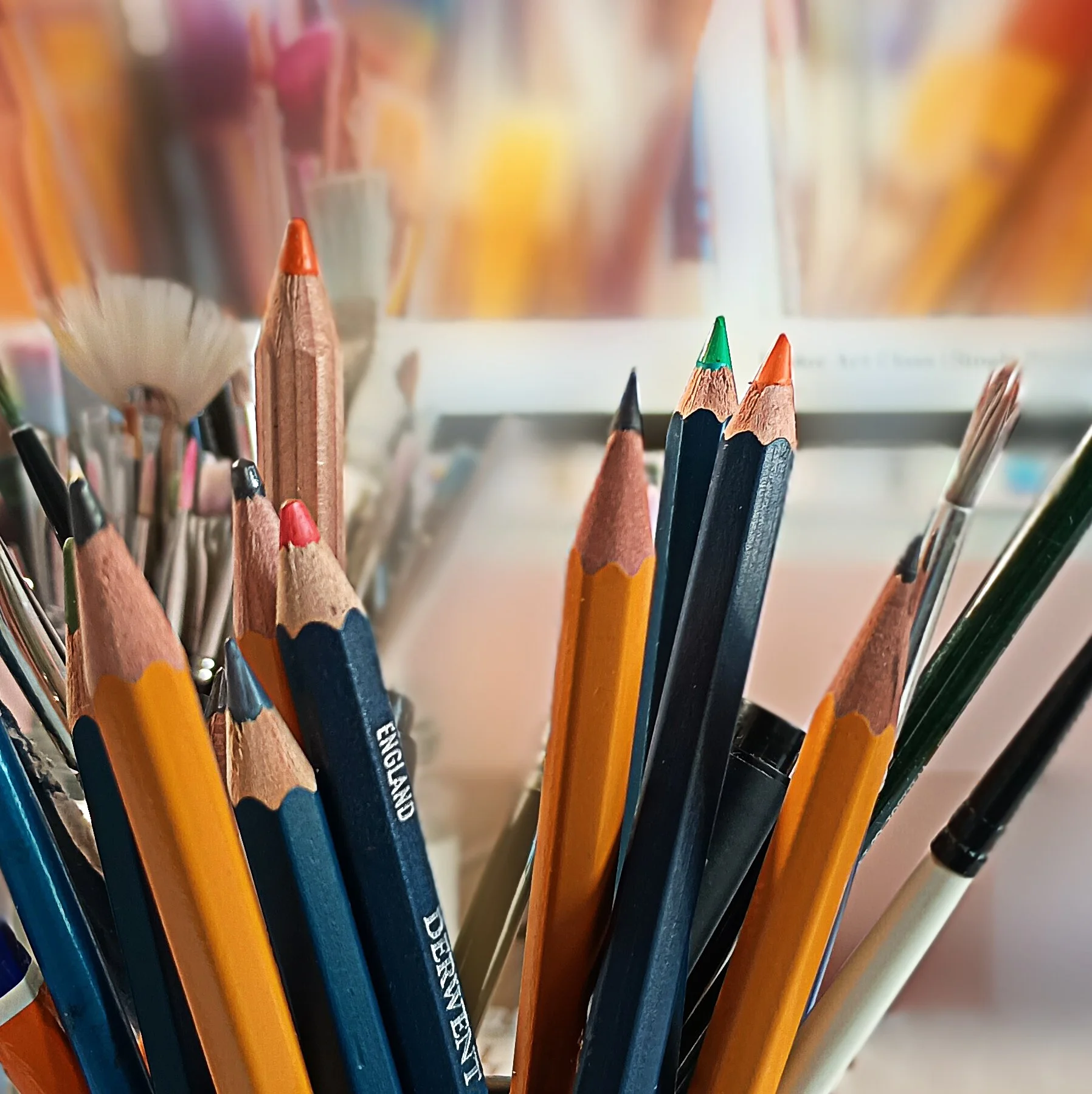 A selection of art paintbrushes and pencils against a blurred background