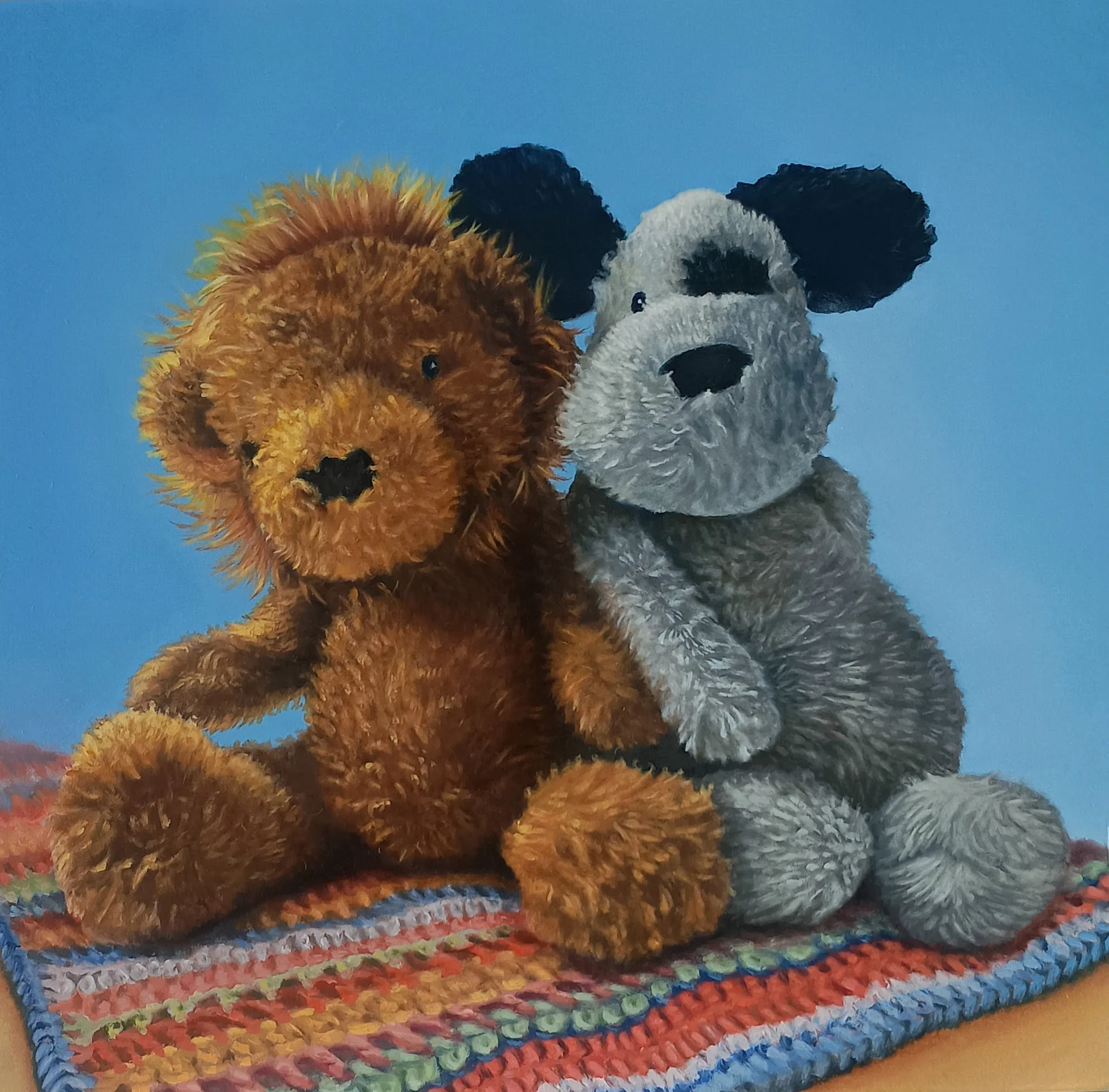 Two plush stuffed animals, a brown dog and a grey and white dog, sitting on a colorful knitted blanket against a blue background.