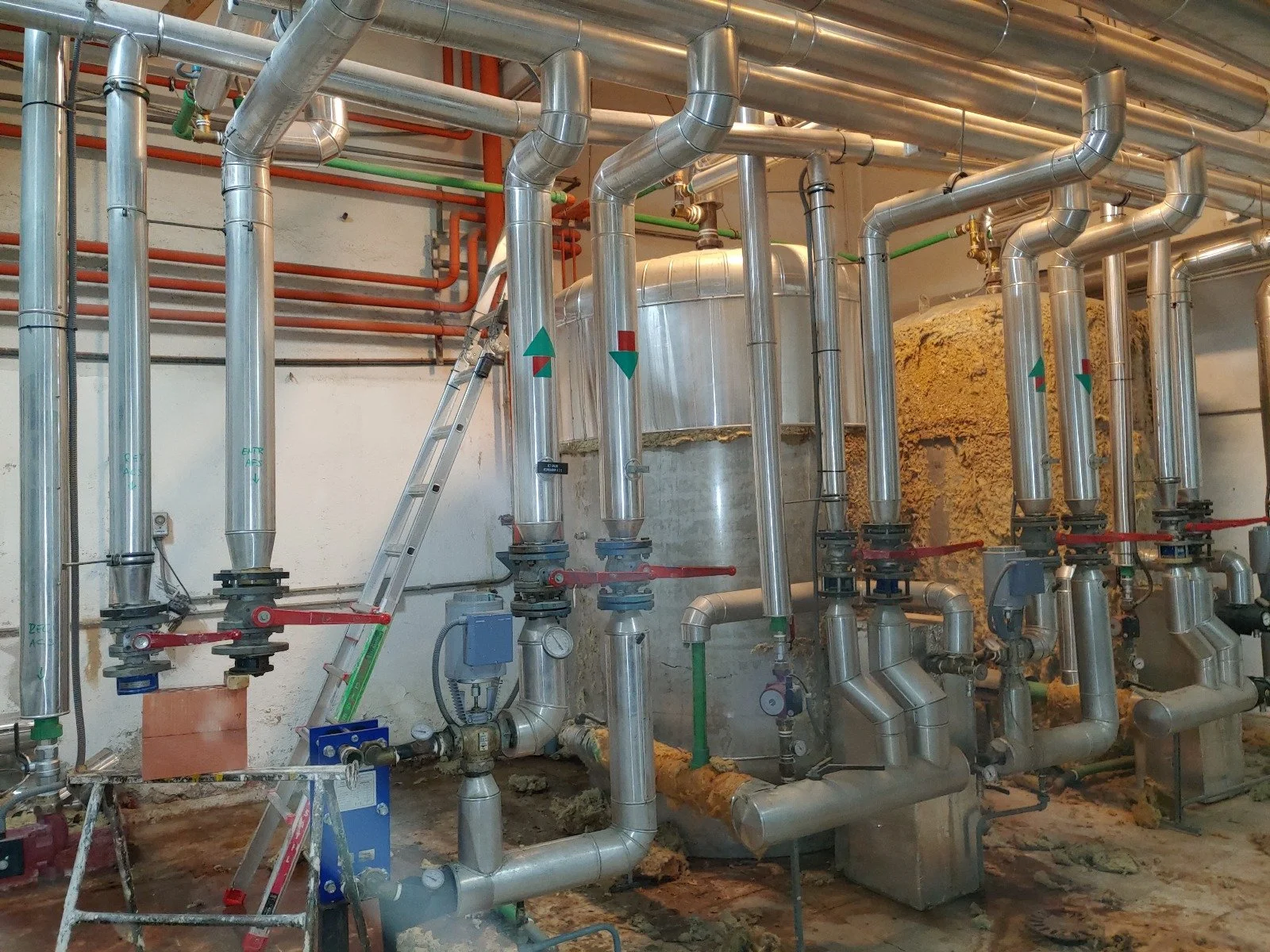 Conjunto de tuberías y válvulas de acero inoxidable en un sistema industrial, con instrumentos de medición y una escalera