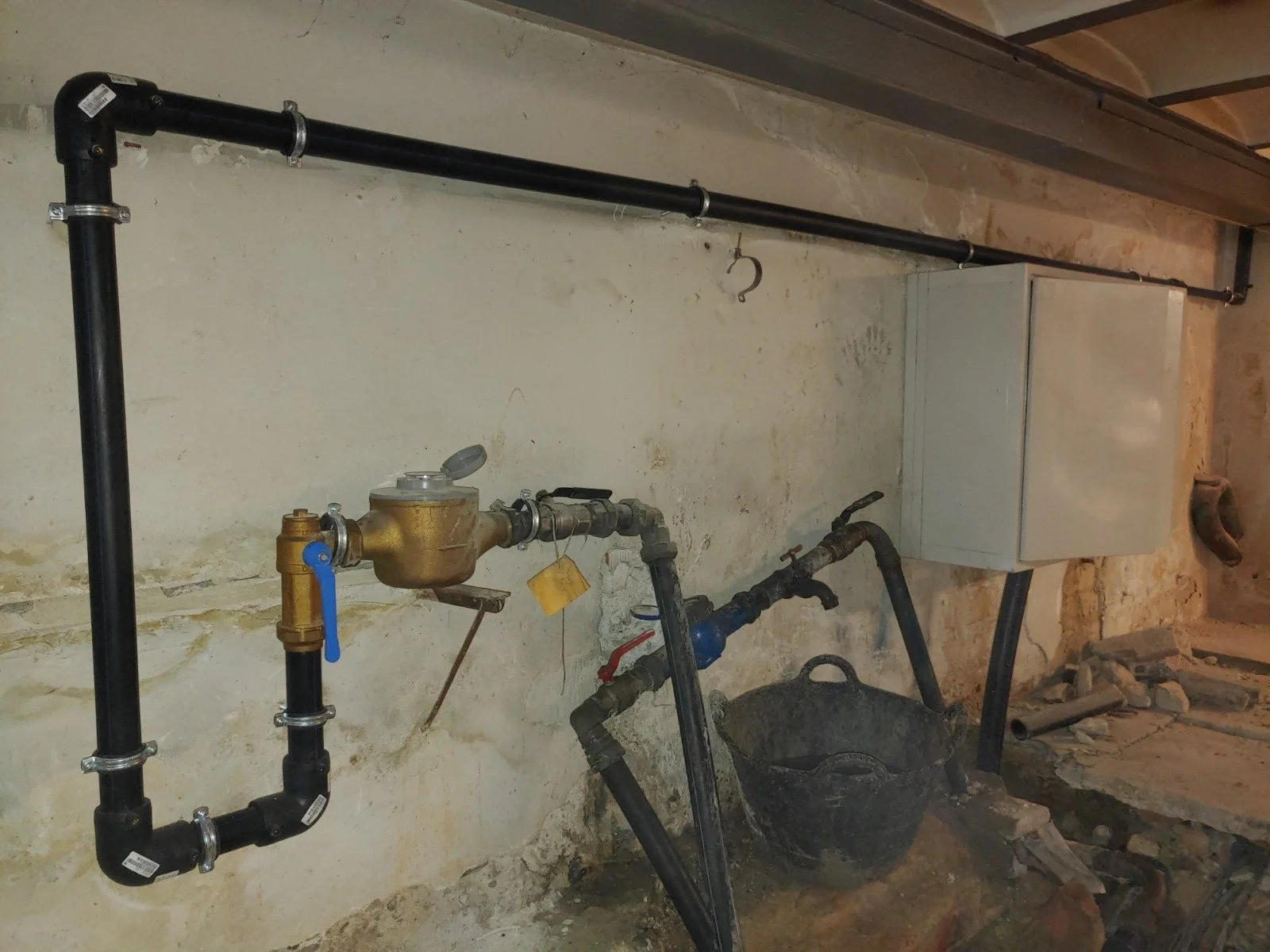 Sistema de plomería y tuberías en una pared de fondo, con una caja de control y una bañera de plástico en un área de construcción o reparación.