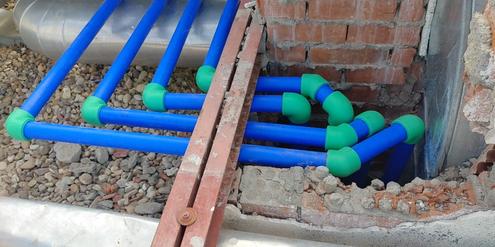 Tuberías de plástico azul y verde instaladas en una excavación para sistema de plomería en construcción.