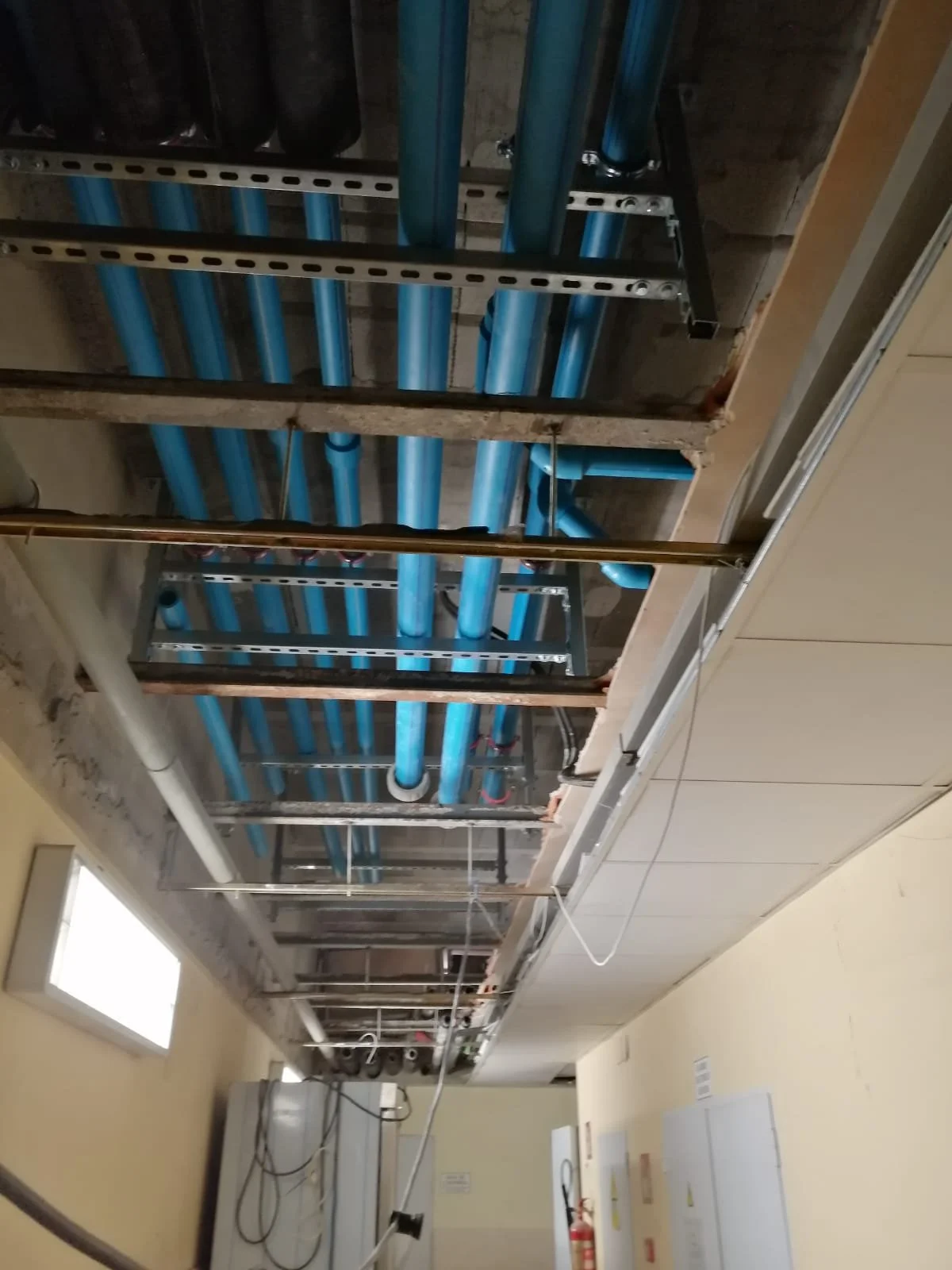 Sistema de tuberías de plomería en construcción, con tuberías azules y estructura metálica en un techo en obra.