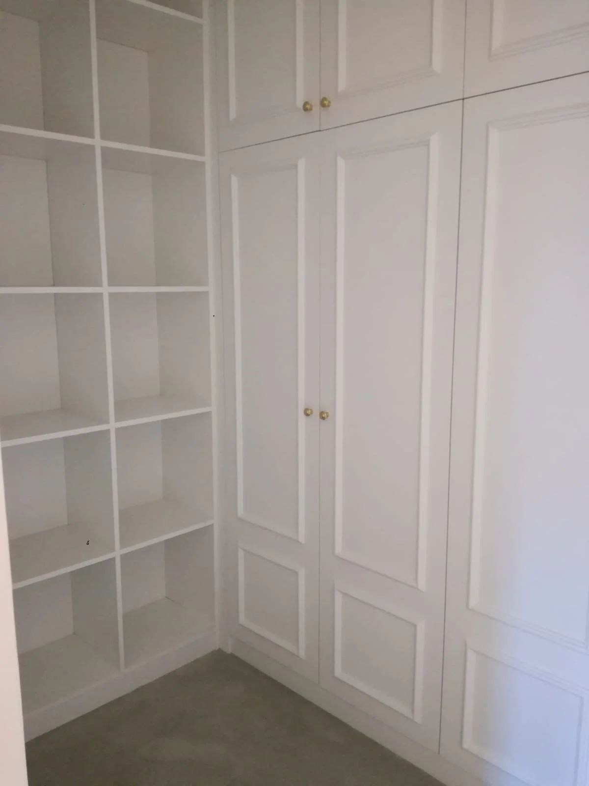 Armario empotrado de madera pintado de blanco con puertas y estanterías en una esquina de una habitación.