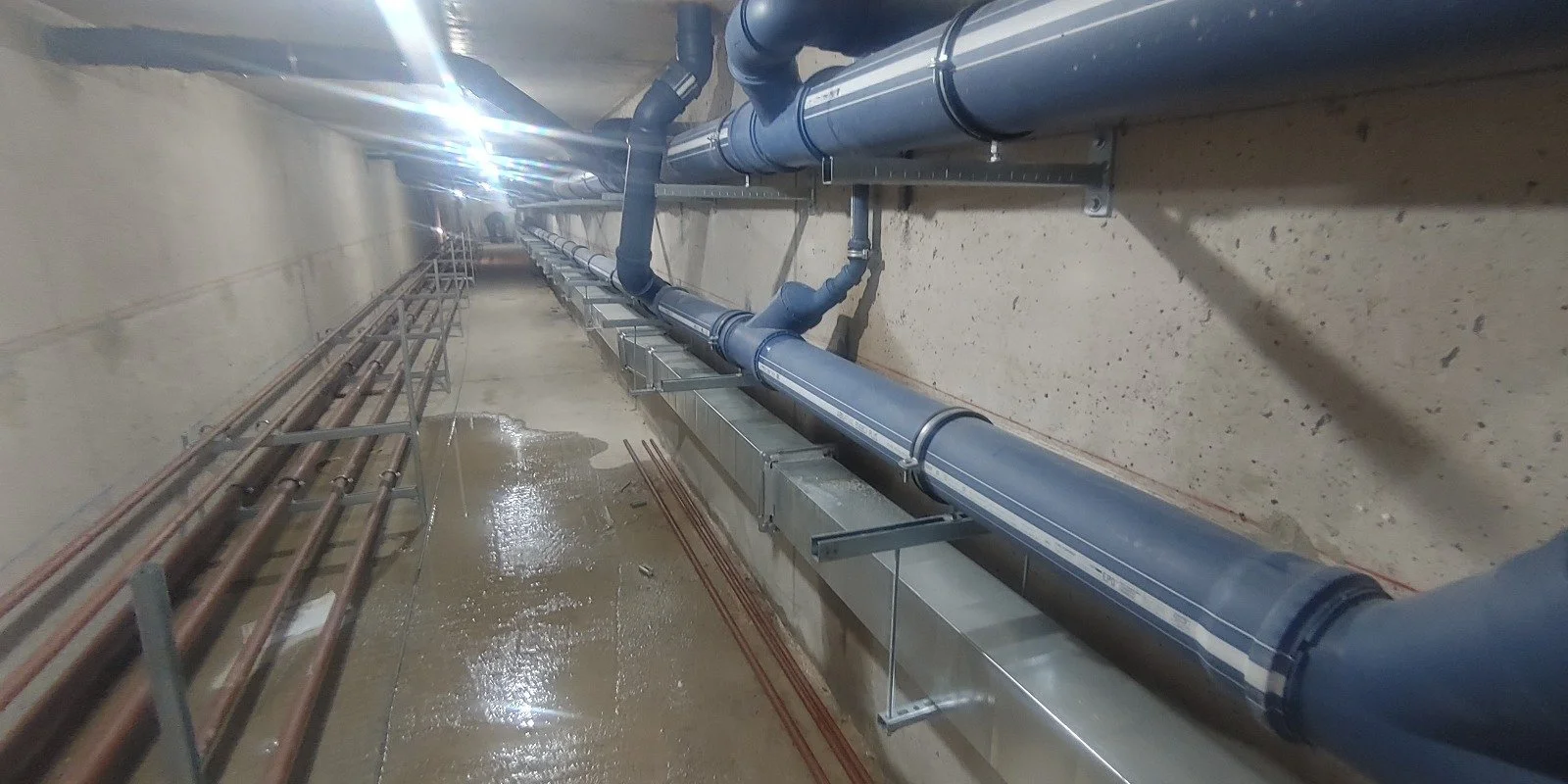 Tuberías de agua en una tubería de servicios de un edificio, instaladas en una pared de concreto con soporte metálico.