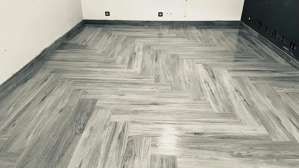 Piso de madera en habitación vacía con paredes blancas y parcialmente gris oscuro.