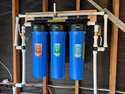 Three blue water filter tanks connected with white pipes and fittings in a plumbing system.