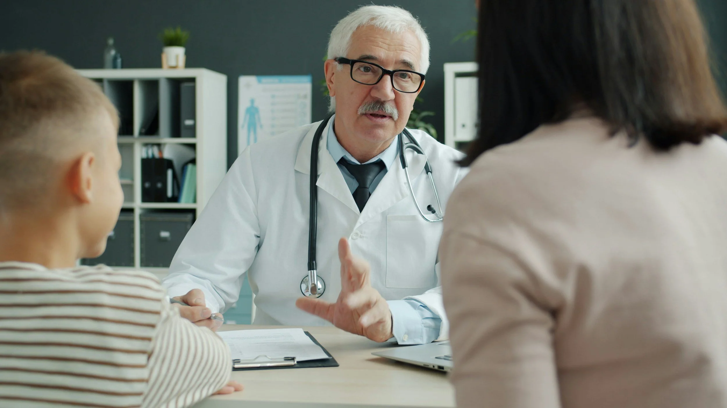 Doctor talking to a woman and a boy in an office or clinic setting.