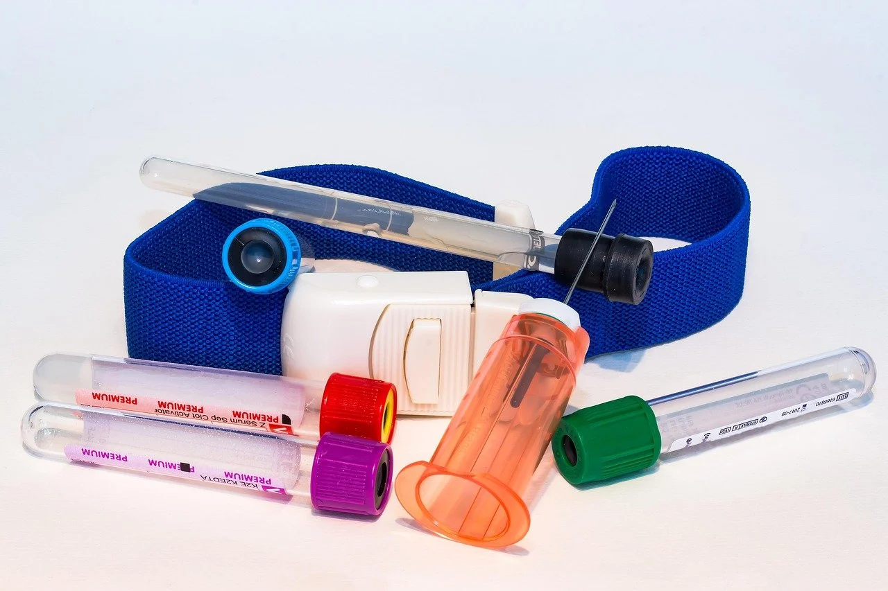 Collection of medical laboratory supplies including test tubes with colored caps, a blue strap, a syringe, and a small white container.
