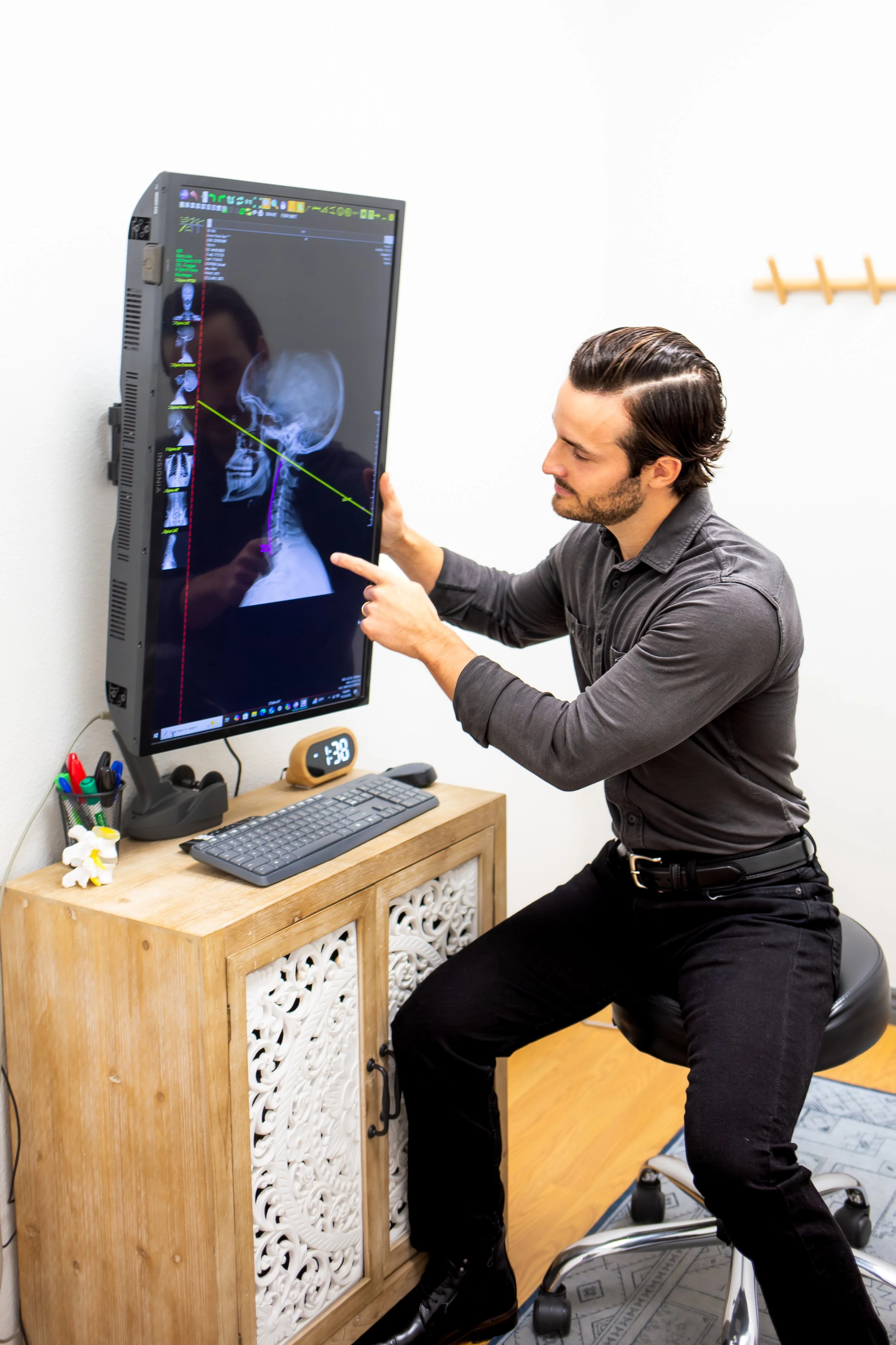 Man displaying a medical X-ray of a head and neck on a vertical monitor in an office setting.