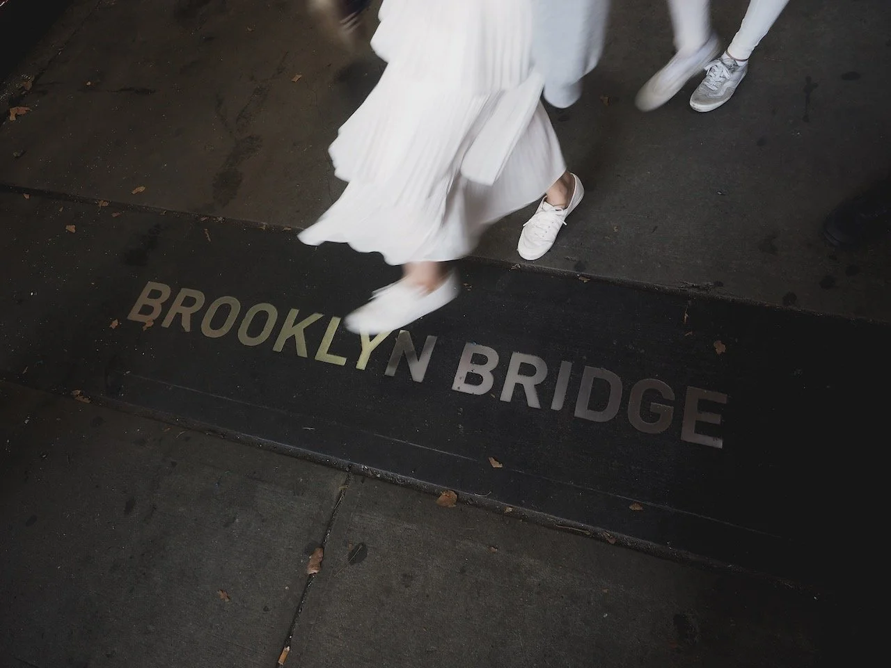 Boden mit der Aufschrift 'Brooklyn Bridge' und Personen, die vorübergehen.